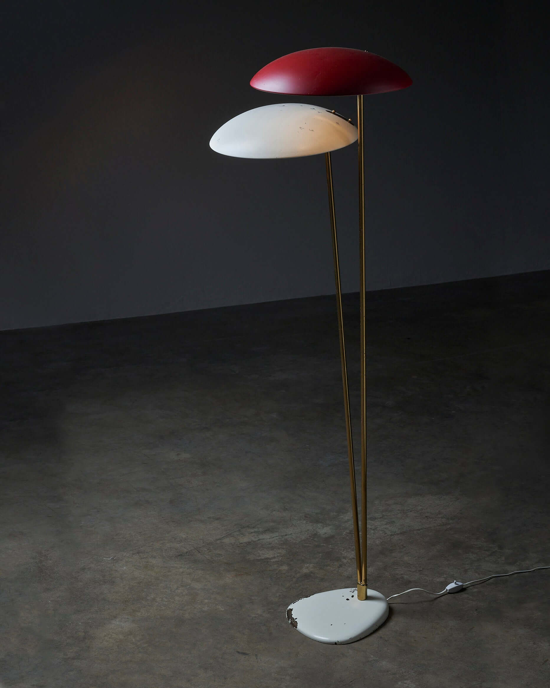 Modern floor lamp with dual red and white shades on gold stand, illuminating a dark interior space.