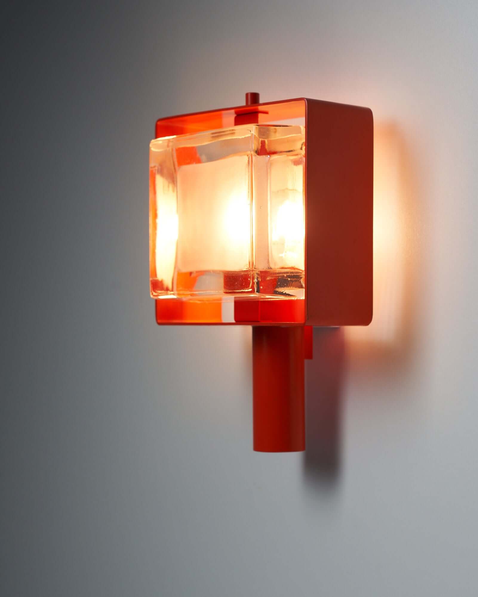Modern orange wall sconce with clear glass shade illuminating a wall.