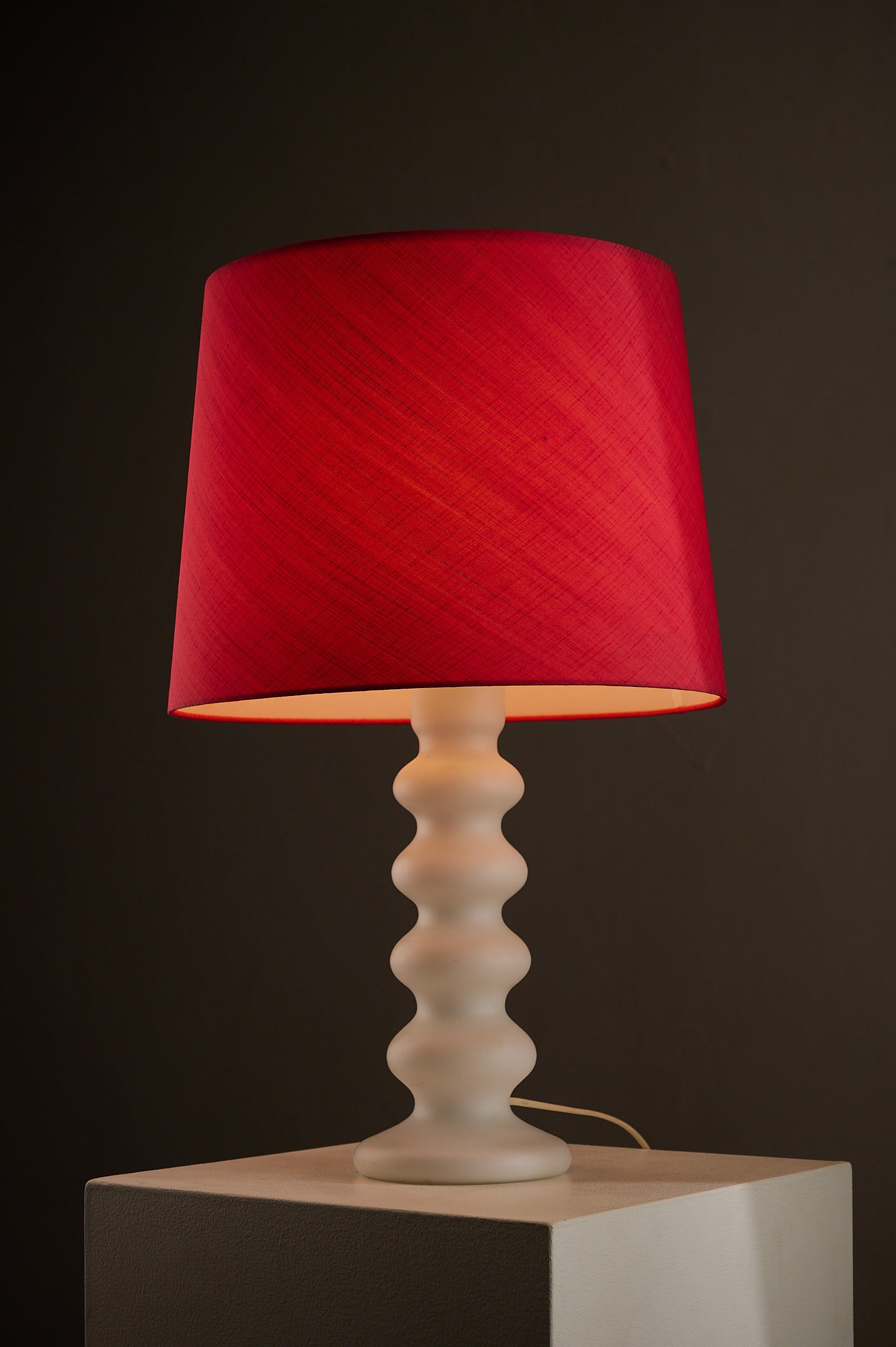 Luxus red lampshade on a white sculptural base illuminating a dark space, showcasing elegant design.