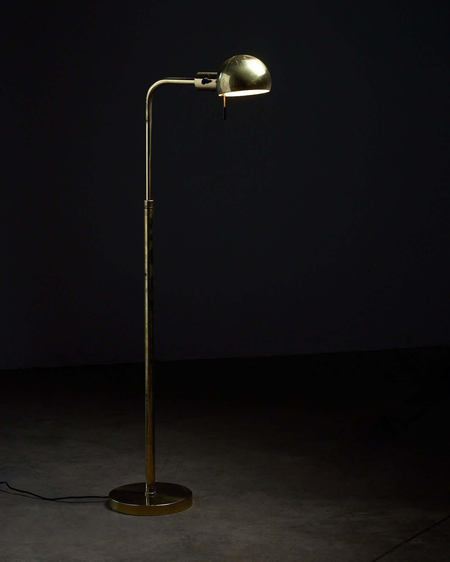 Metalarte floor lamp in polished brass, 1970s standing on a dark background with a hemispherical shade.