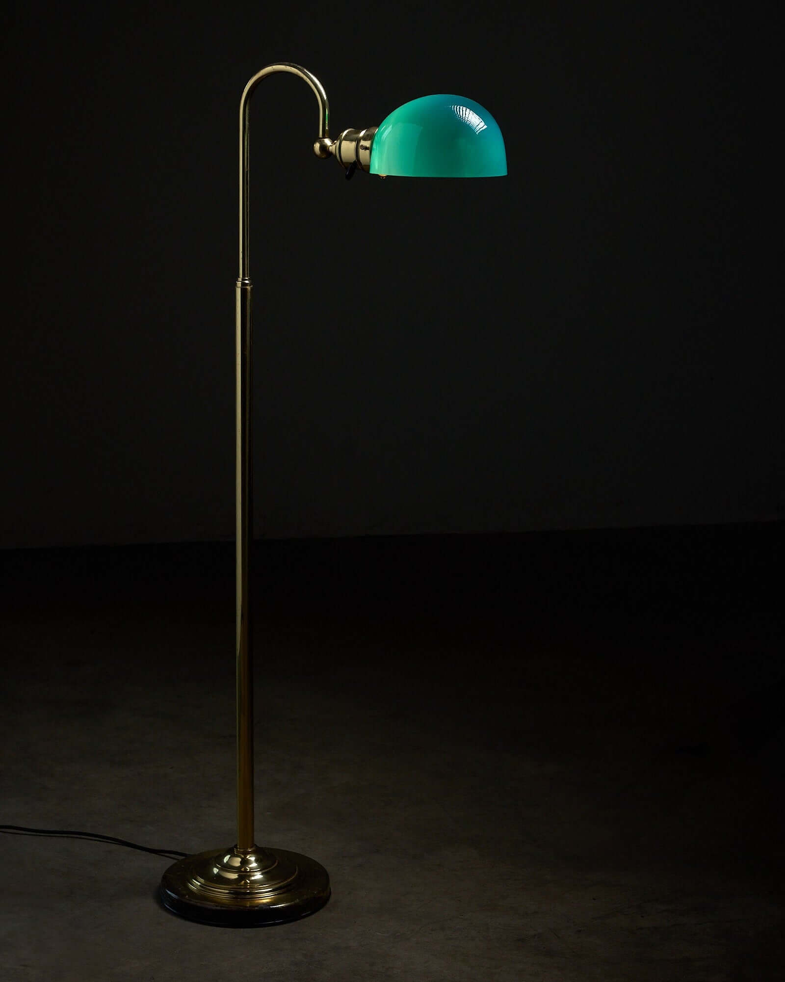 Floor lamp in brass with green glass shade, 1970s illuminating a dark space.