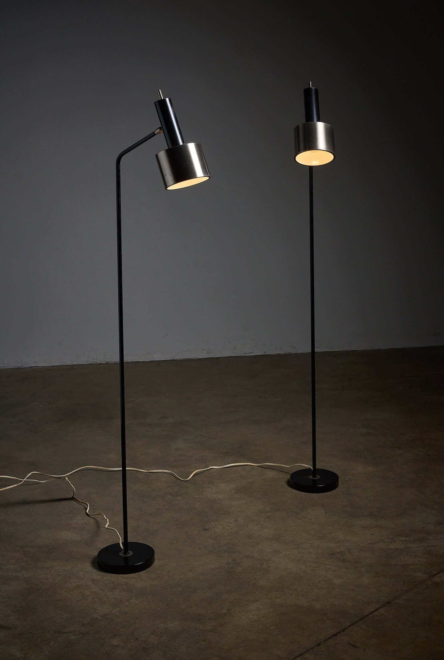 Pair of floor lamps in black metal with brushed aluminum shades, 1970s on a concrete floor.