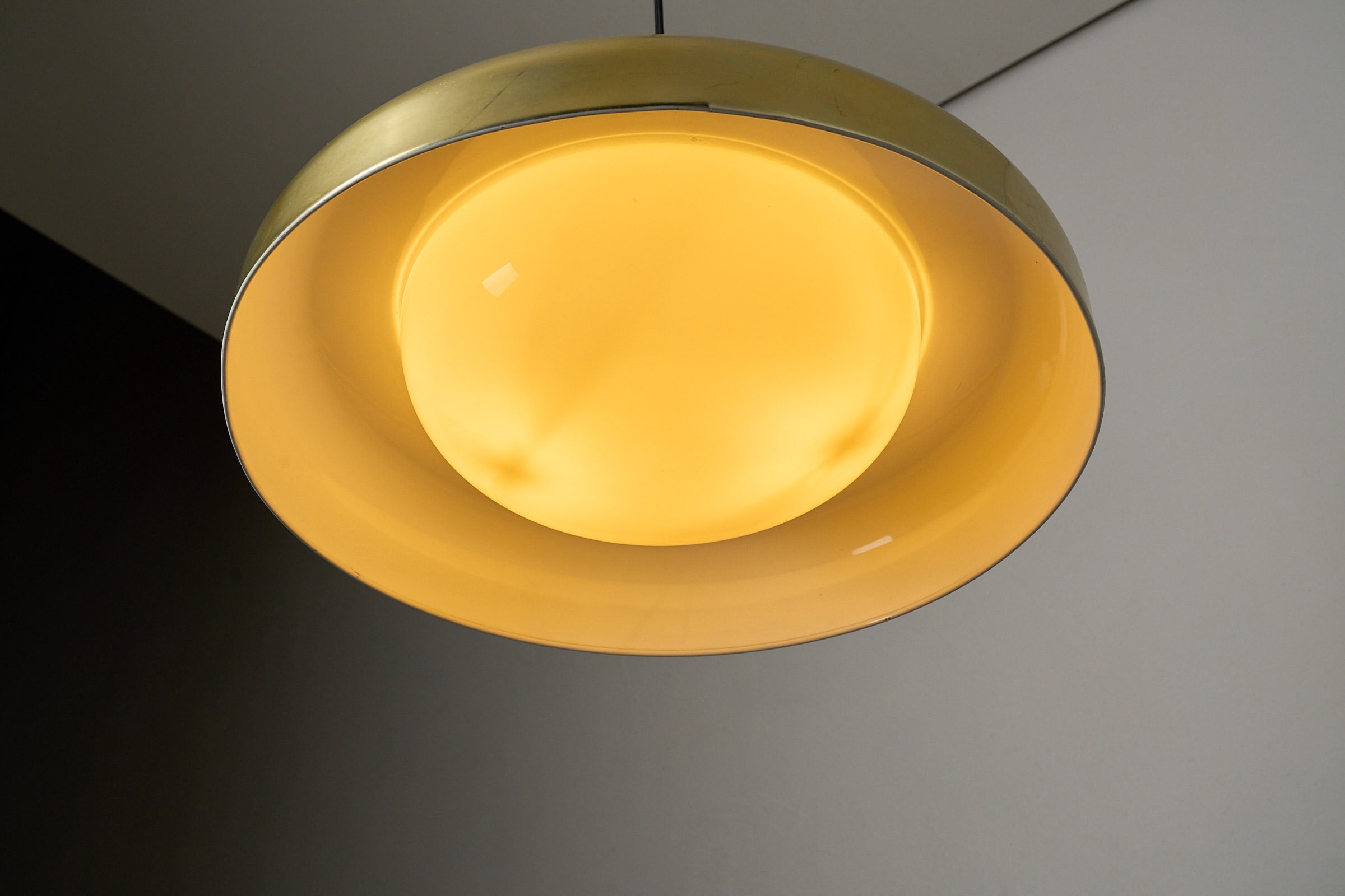 Large Brass and Yellow Glass Pendant illuminated overhead with soft yellow glow and sleek design.