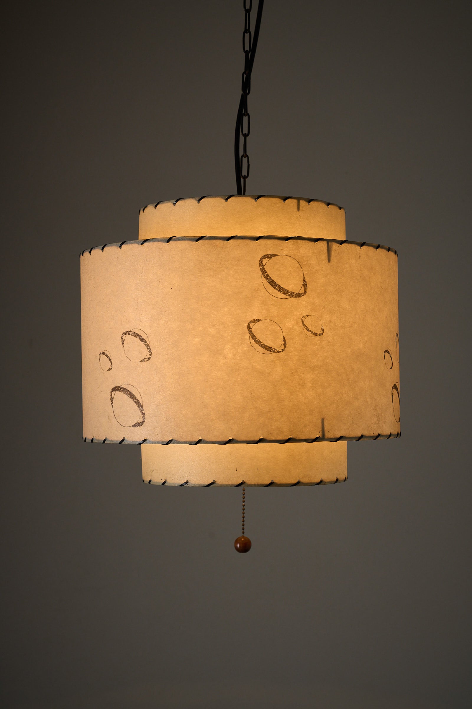 Parchment Pendant Lamp by Archaic Smile Inc, double-tiered shade with planet pattern, hanging in a room.