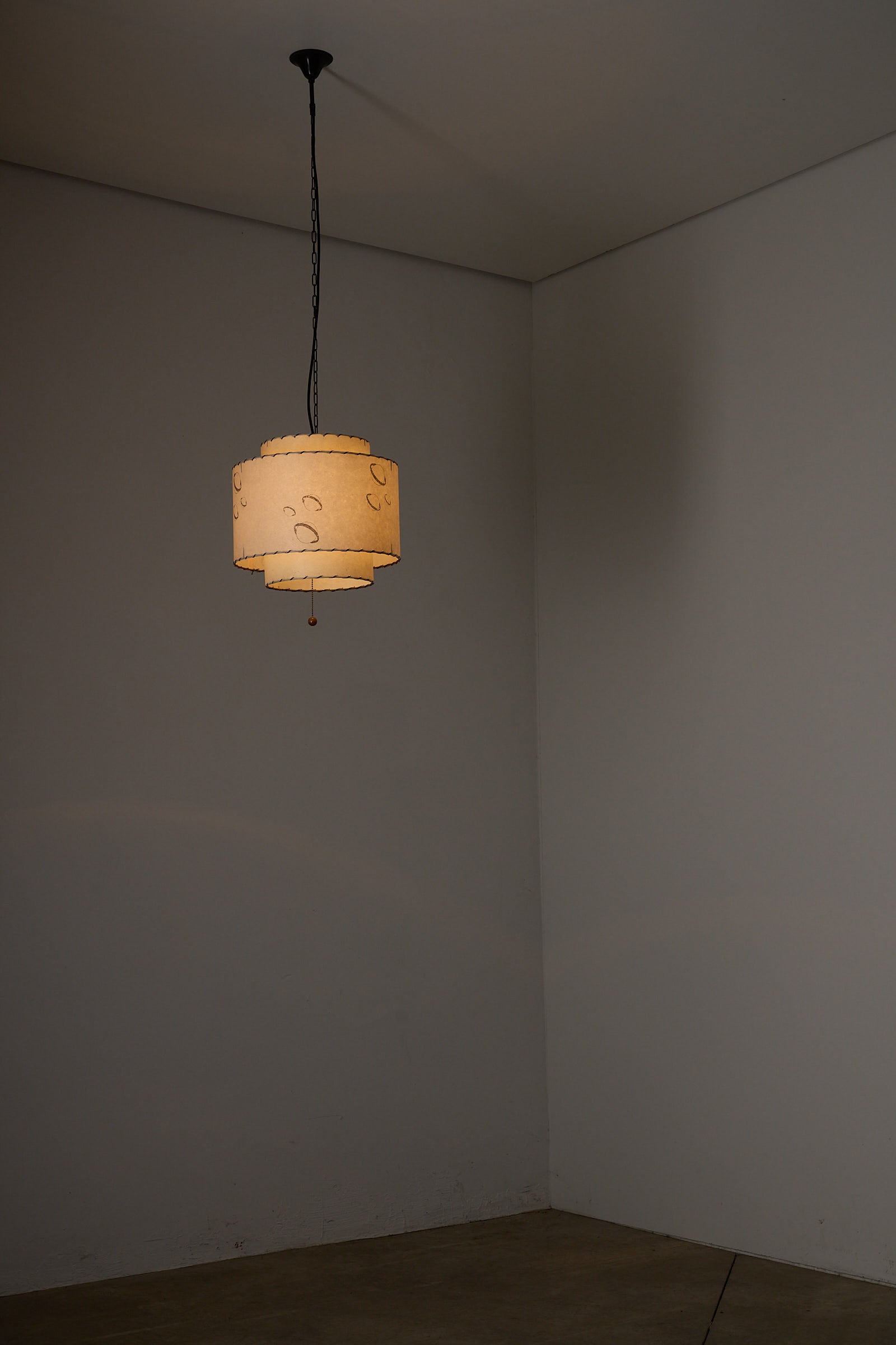 Parchment Pendant Lamp by Archaic Smile Inc hanging in a minimalist room, featuring a planetary motif and warm light.