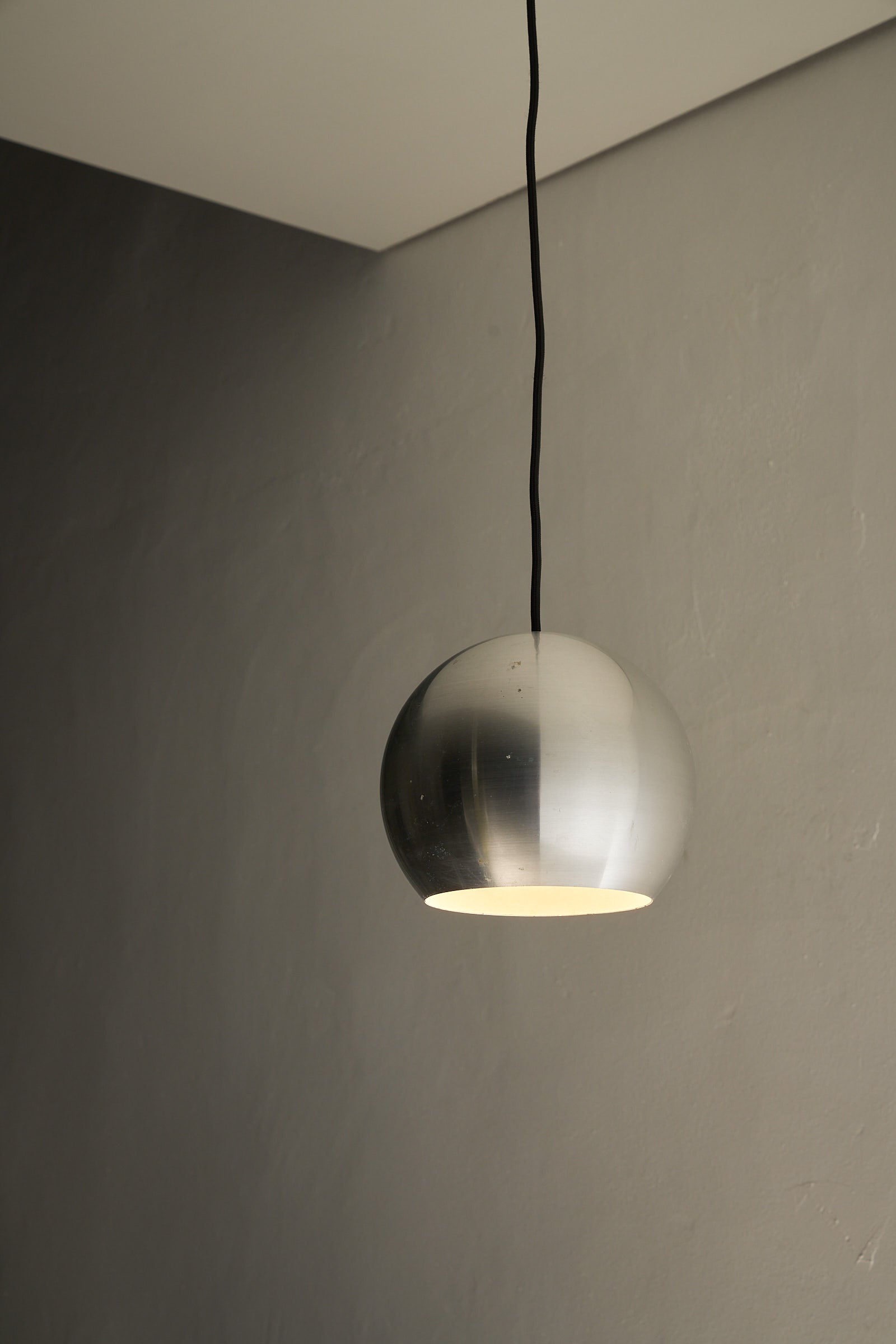 Brushed Aluminium Sphere Pendant hanging from the ceiling, illuminating a modern interior.