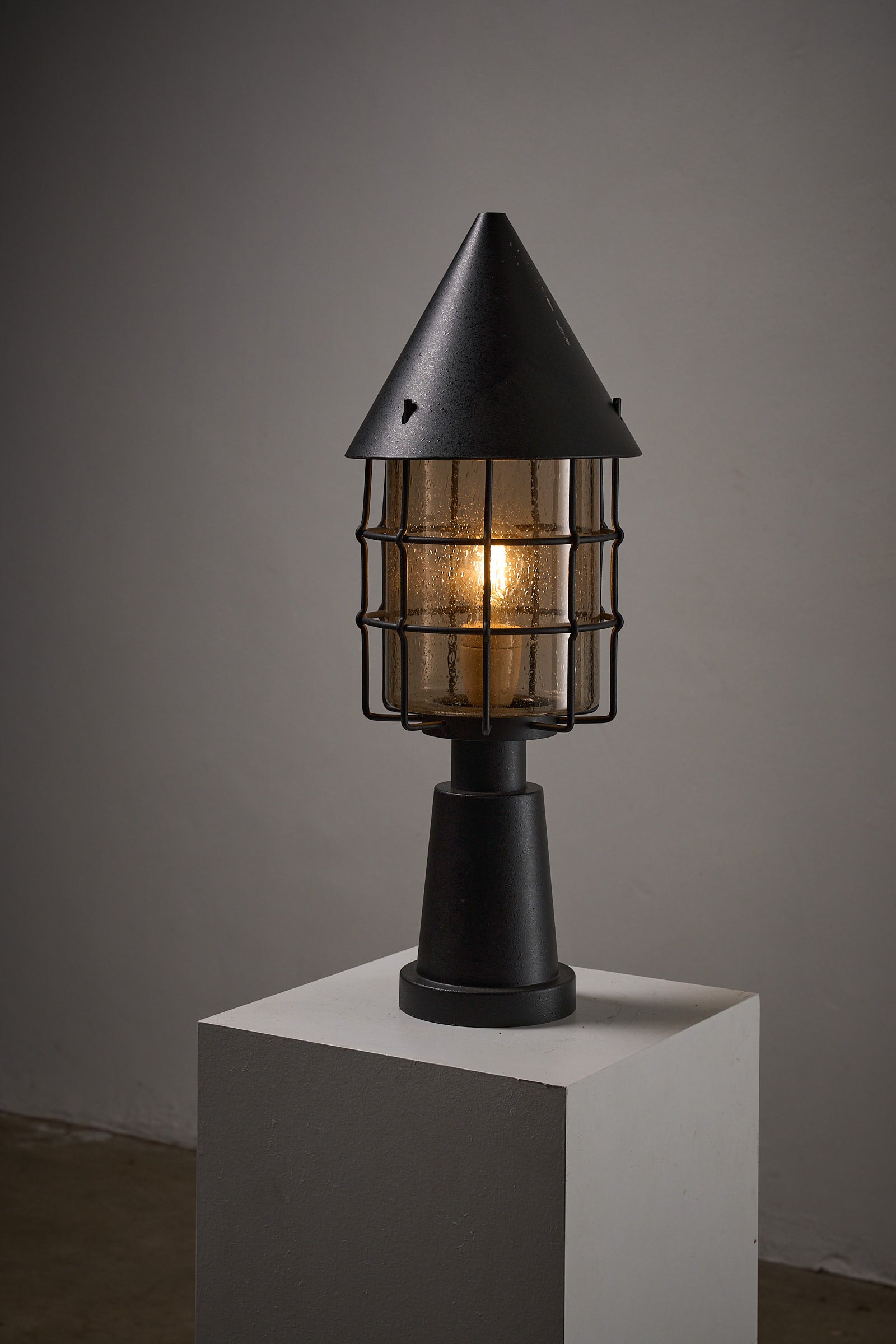 Outdoor Lantern by Boom BEGA displayed on a pedestal with a glowing light, showcasing its architectural design.