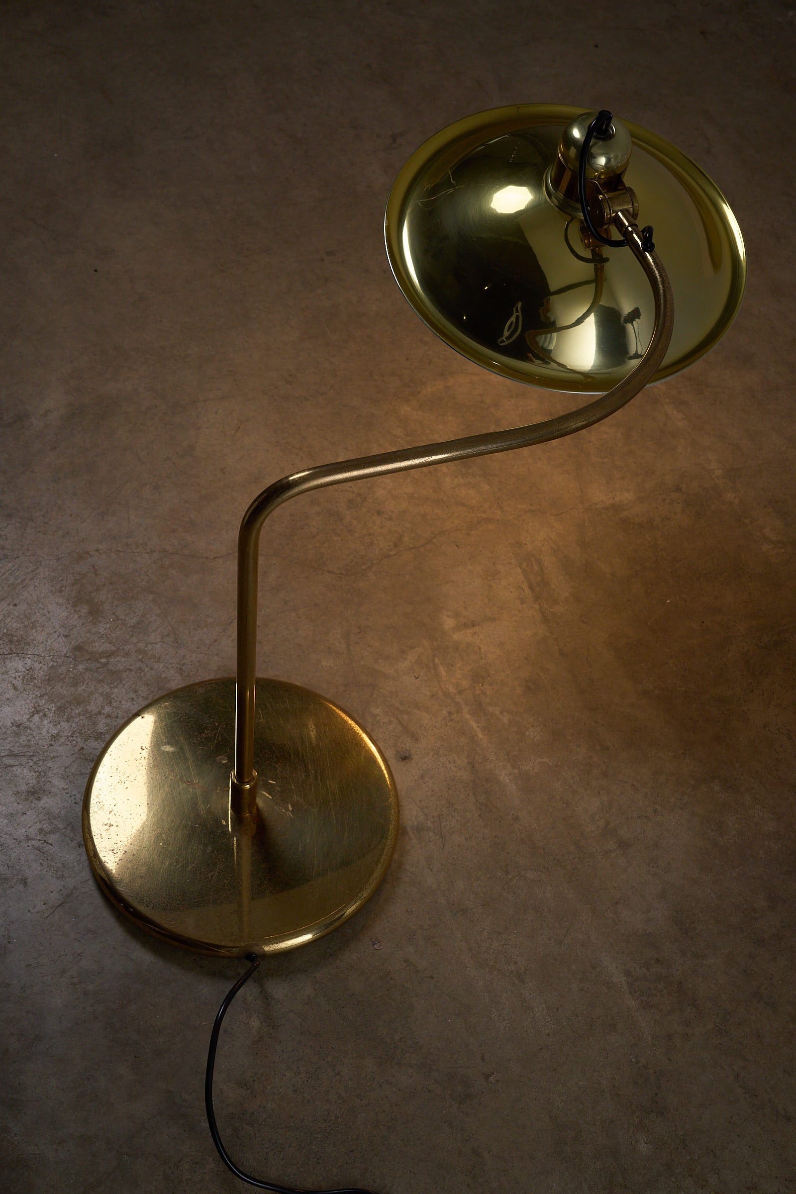 Cosack Brass Table Lamp with Curved Arm casting a warm glow, showcasing mid-century design and polished brass finish.