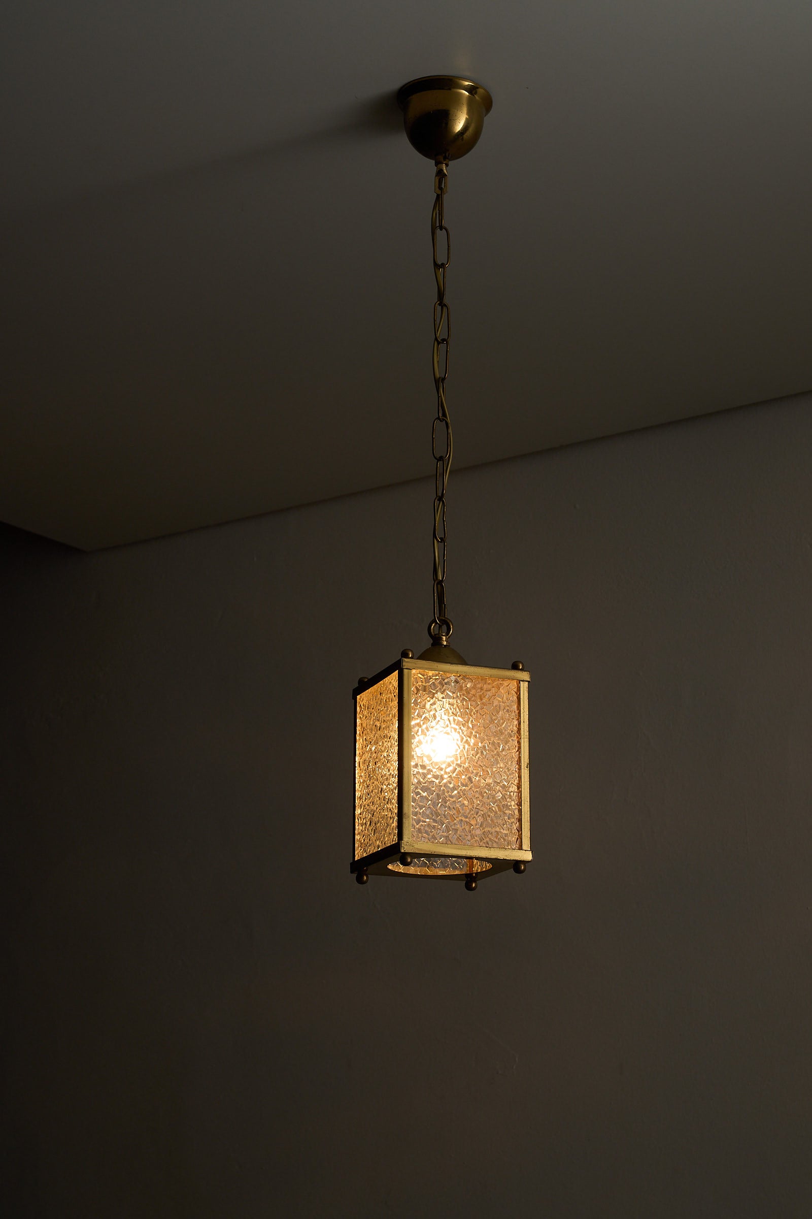 Mid-Century Brass Pendant Lamp with Textured Glass Shade hanging from a chain, illuminating a warm ambiance.