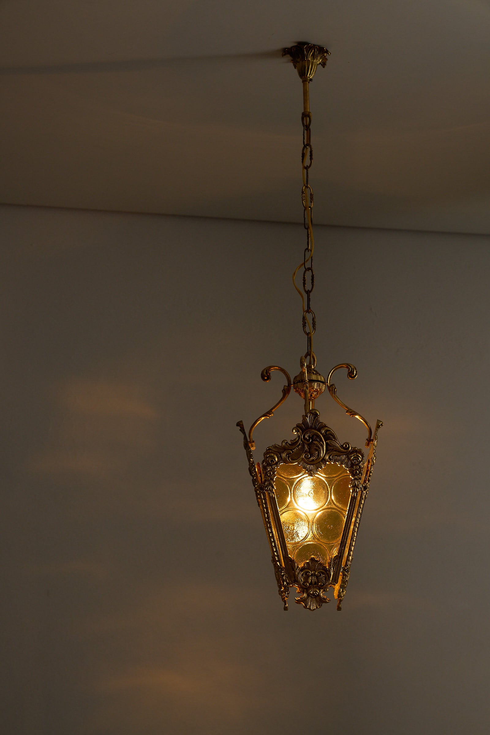 Rococo-Style Gilt Pendant Lamp with Structured Amber Glass hanging from a chain, illuminating softly in a room.