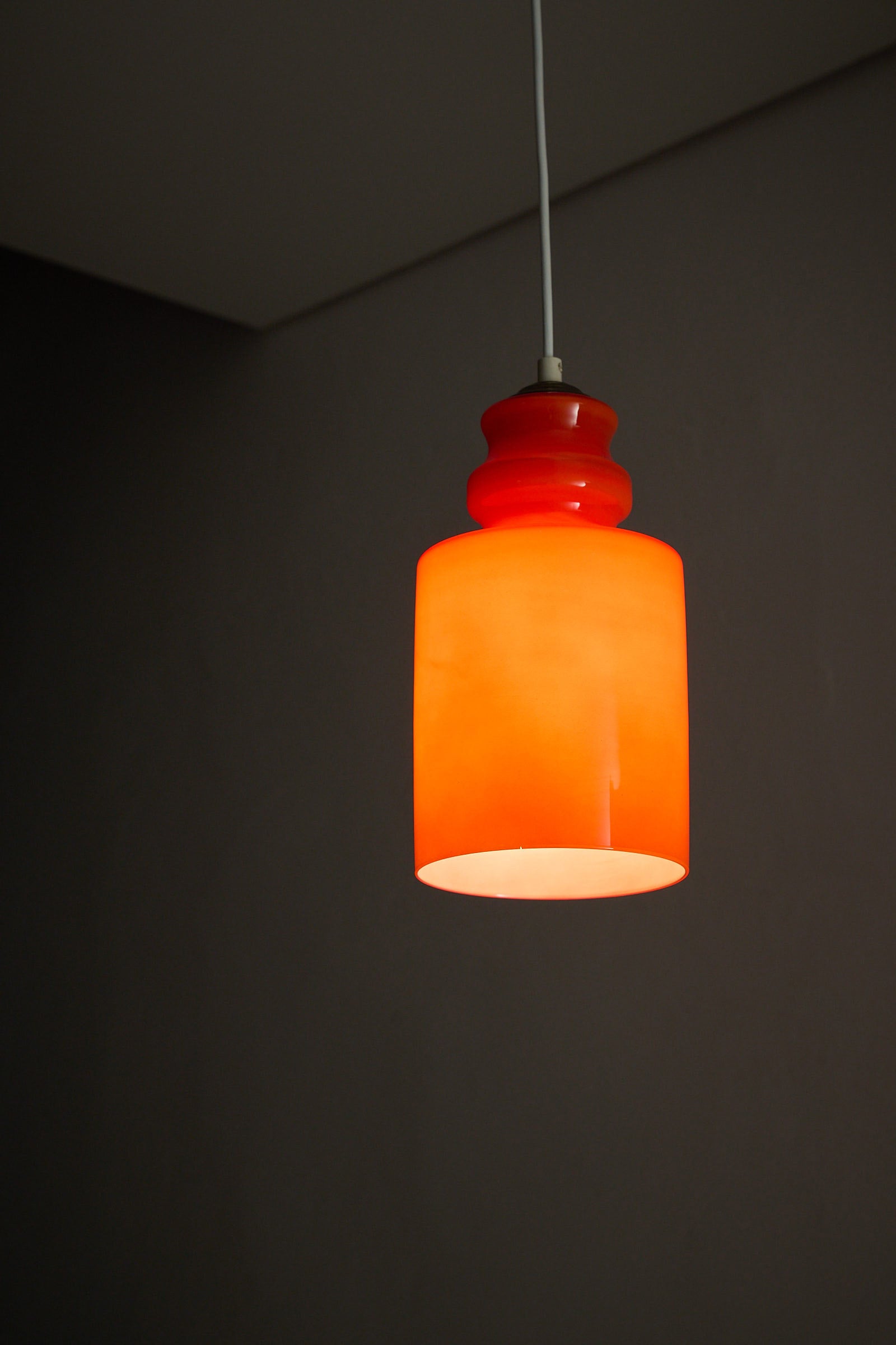 Orange Glass Pendant Lamp hanging from the ceiling with a glossy shade in warm tones.