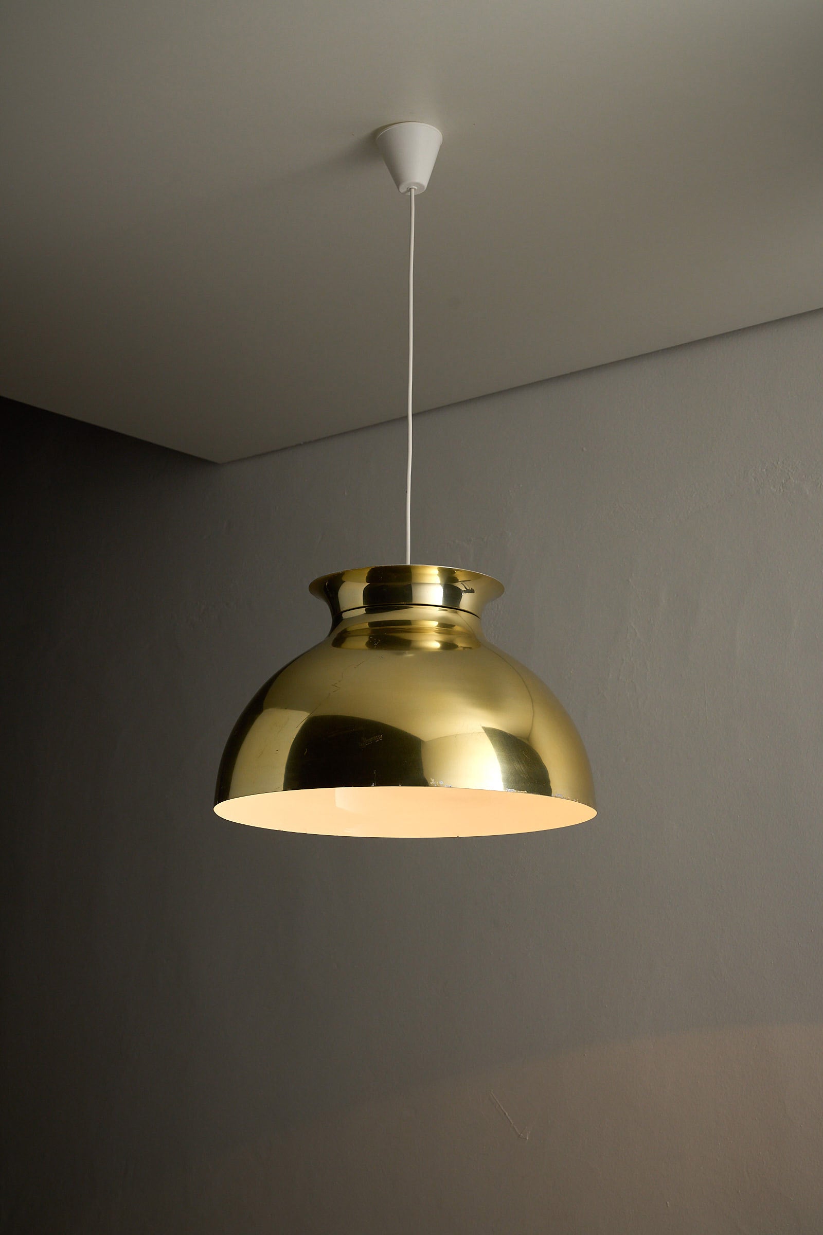 Large Brass Dome Pendant suspended from a white cable, featuring a polished brass shade and white interior.