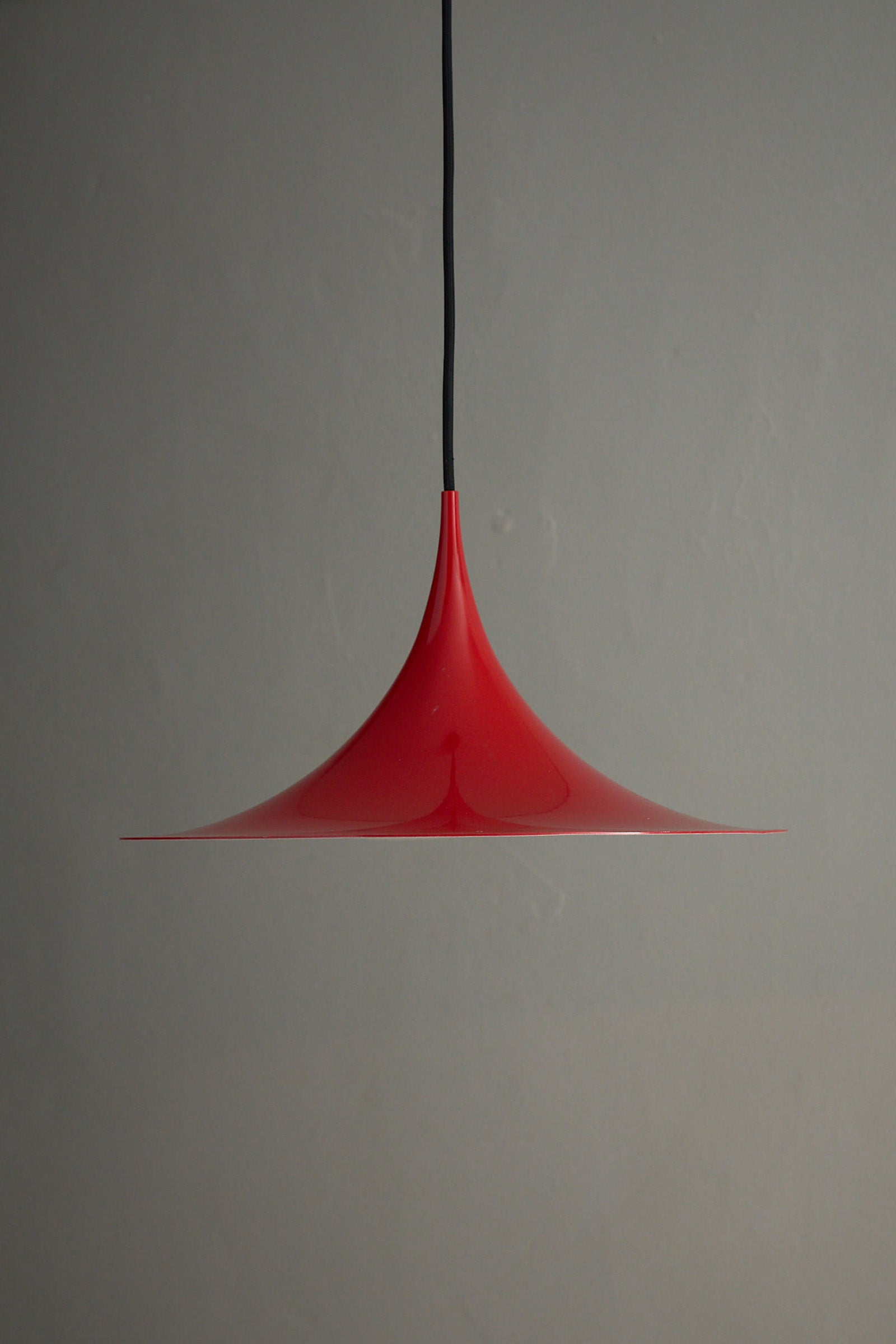 Fog&Mørup Red Semi Pendant Lamp hanging against a gray background, showcasing its sleek design and vibrant red color.