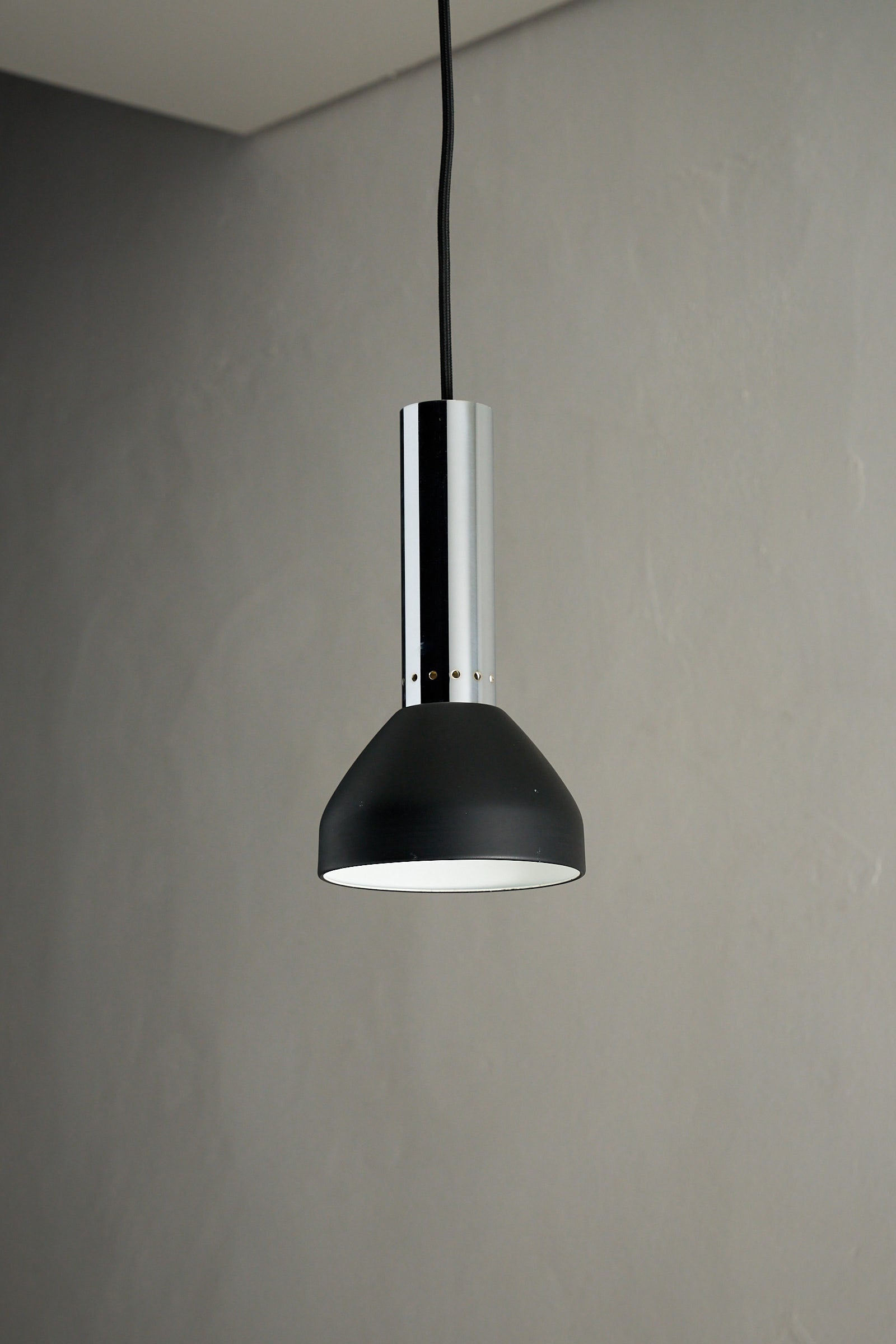Chrome and Black Pendant Lamp with Perforated Detail hanging over a smooth grey surface, showcasing its modern design.