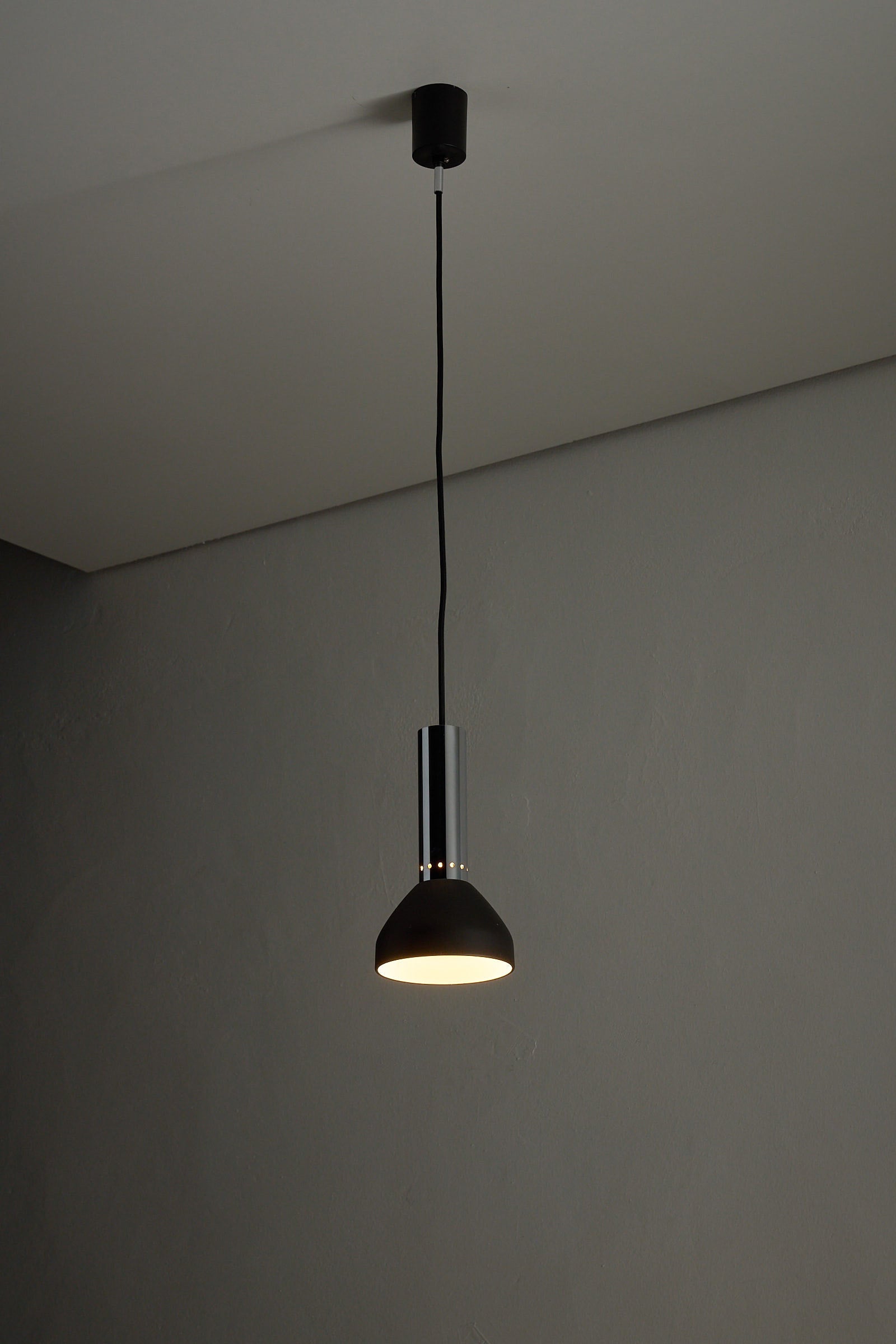 Chrome and Black Pendant Lamp with Perforated Detail hanging against a plain wall, showcasing its elegant design.