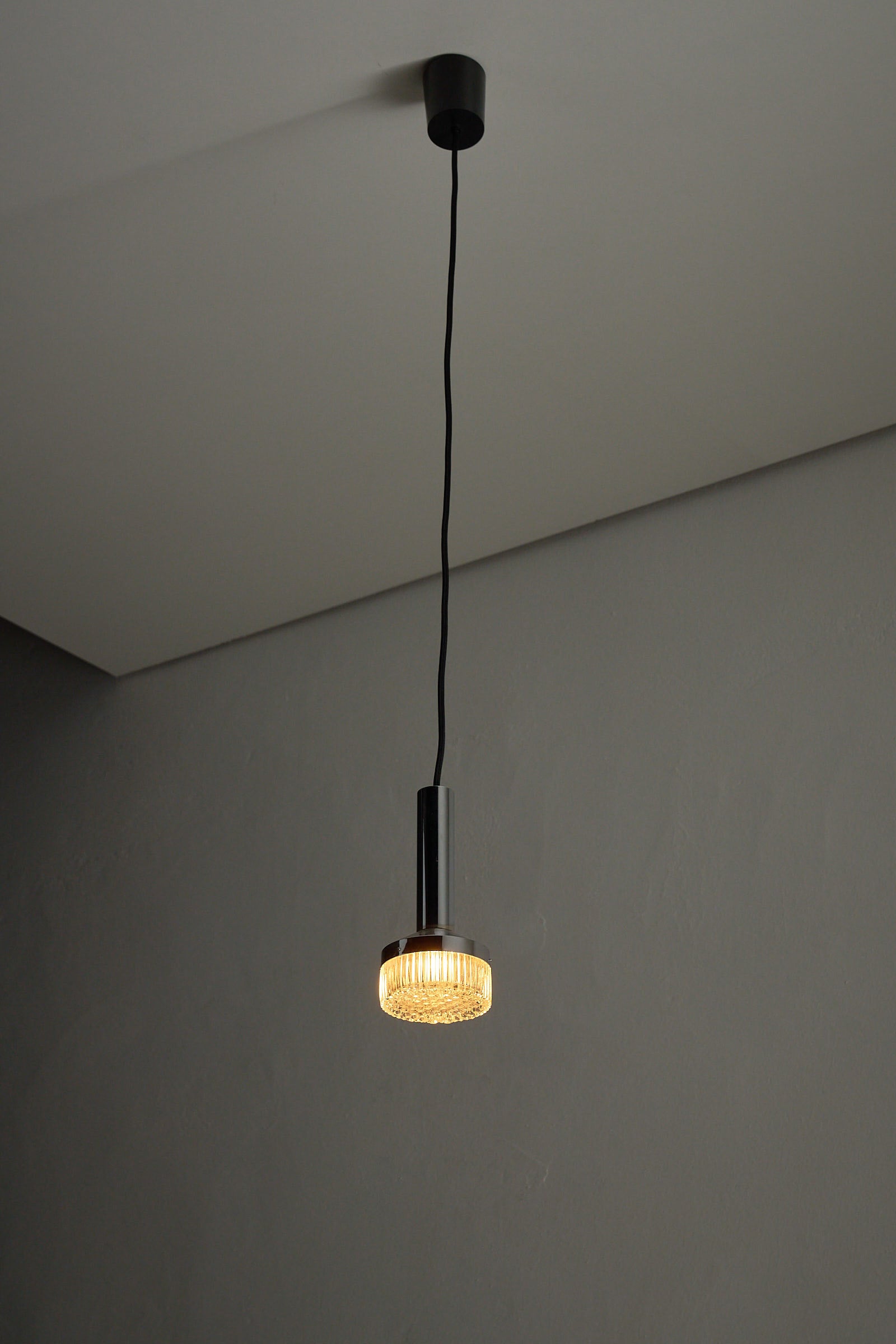 Chrome Pendant Lamp With Textured Glass Diffuser hanging from ceiling with warm light.