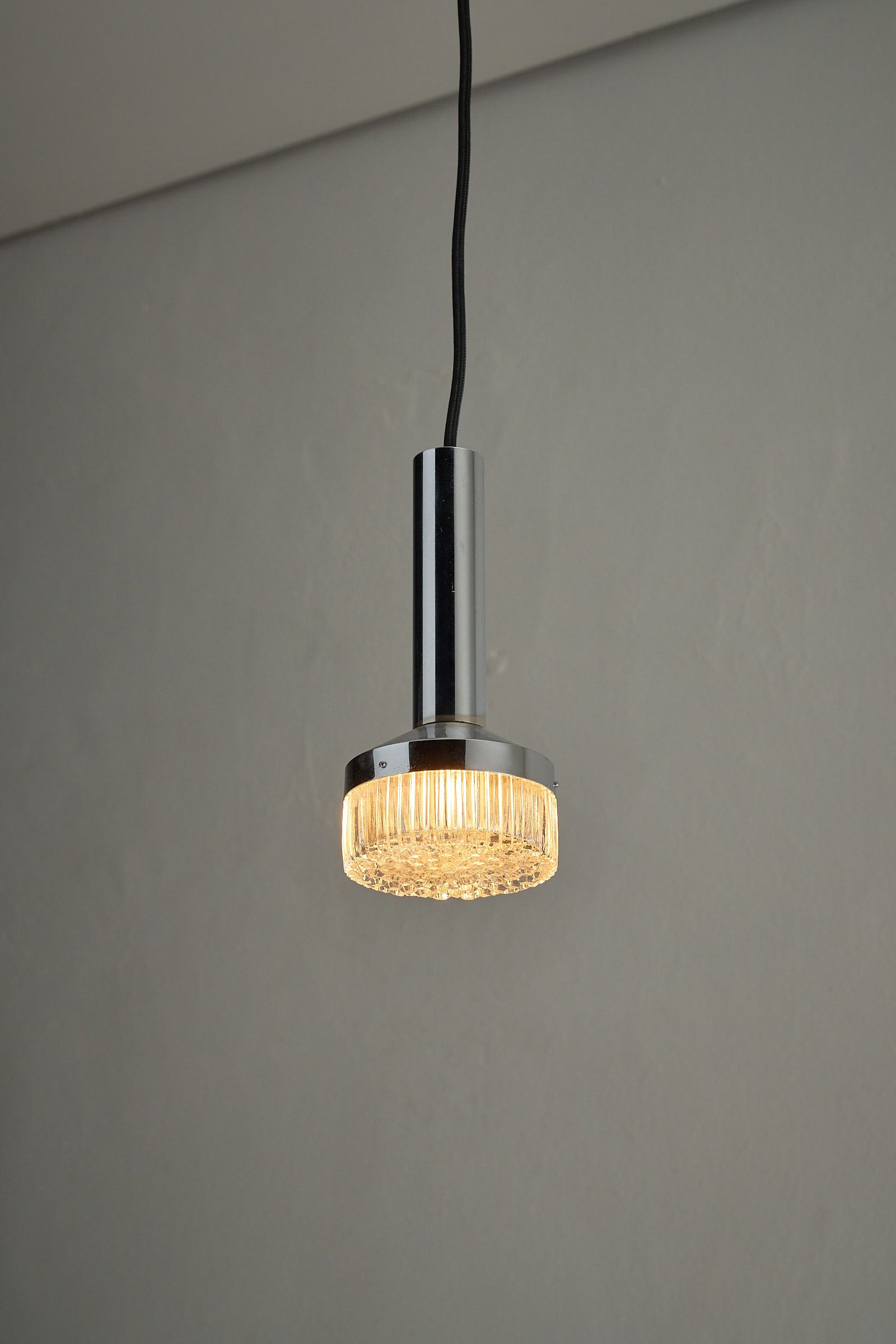 Chrome Pendant Lamp With Textured Glass Diffuser hanging from a ceiling, illuminated with a warm glow.