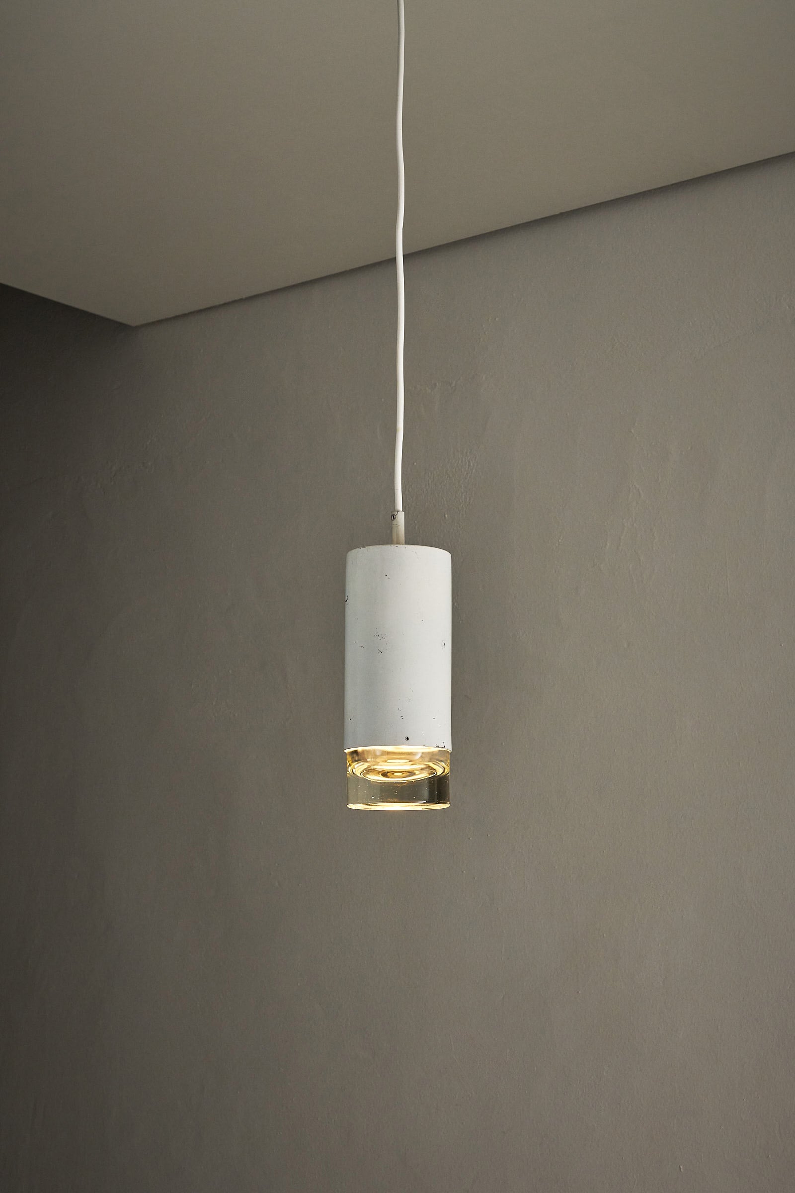 RAAK Amsterdam White Cylinder and Solid Glass Pendant Light hanging against a gray wall.