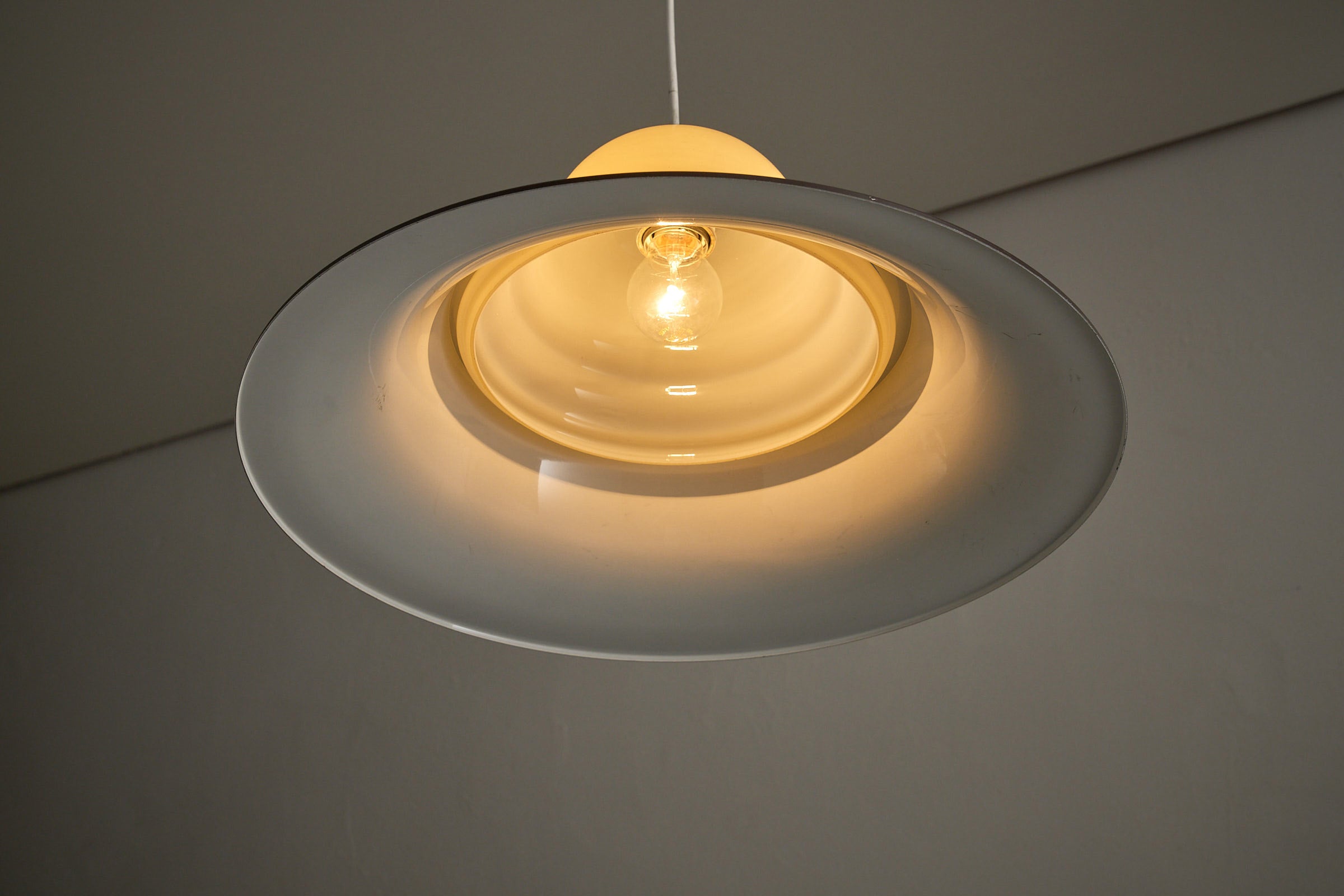 Mid-Century Modern Brown and Opaline Glass Layered Pendant hanging with soft amber light.