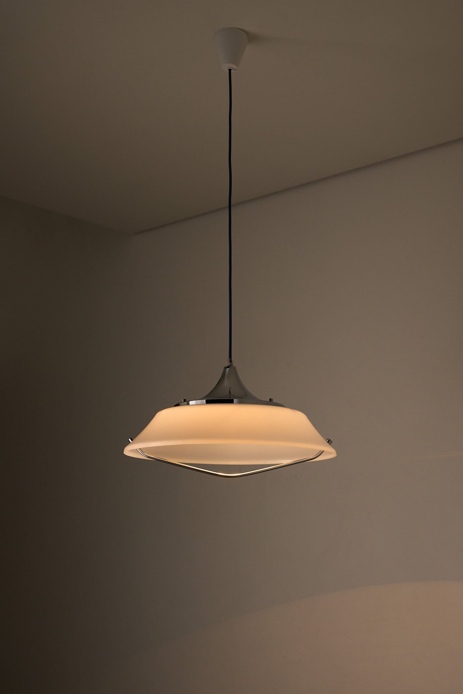 Mid-Century Modern White Acrylic Dish Pendant with Chrome Yoke hanging in softly lit room.