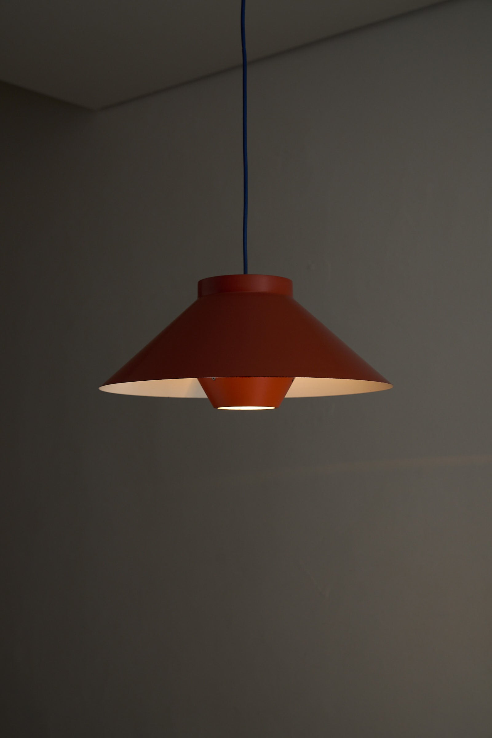 1960s Functionalist Layered Pendant Lamp in Stone Red hanging with conical shade and blue cord against a neutral wall.