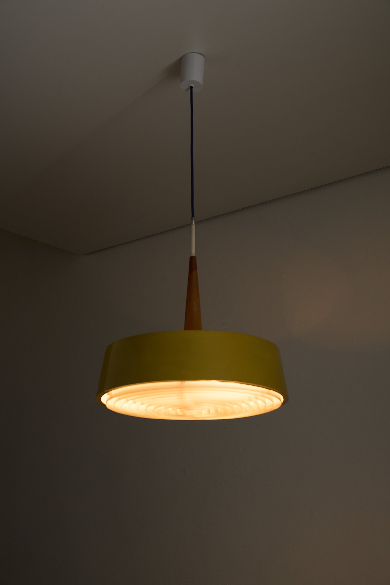 Pendant Lamp in Yellow with Teak Accent hanging from the ceiling, showcasing a modern design and warm uplighting.