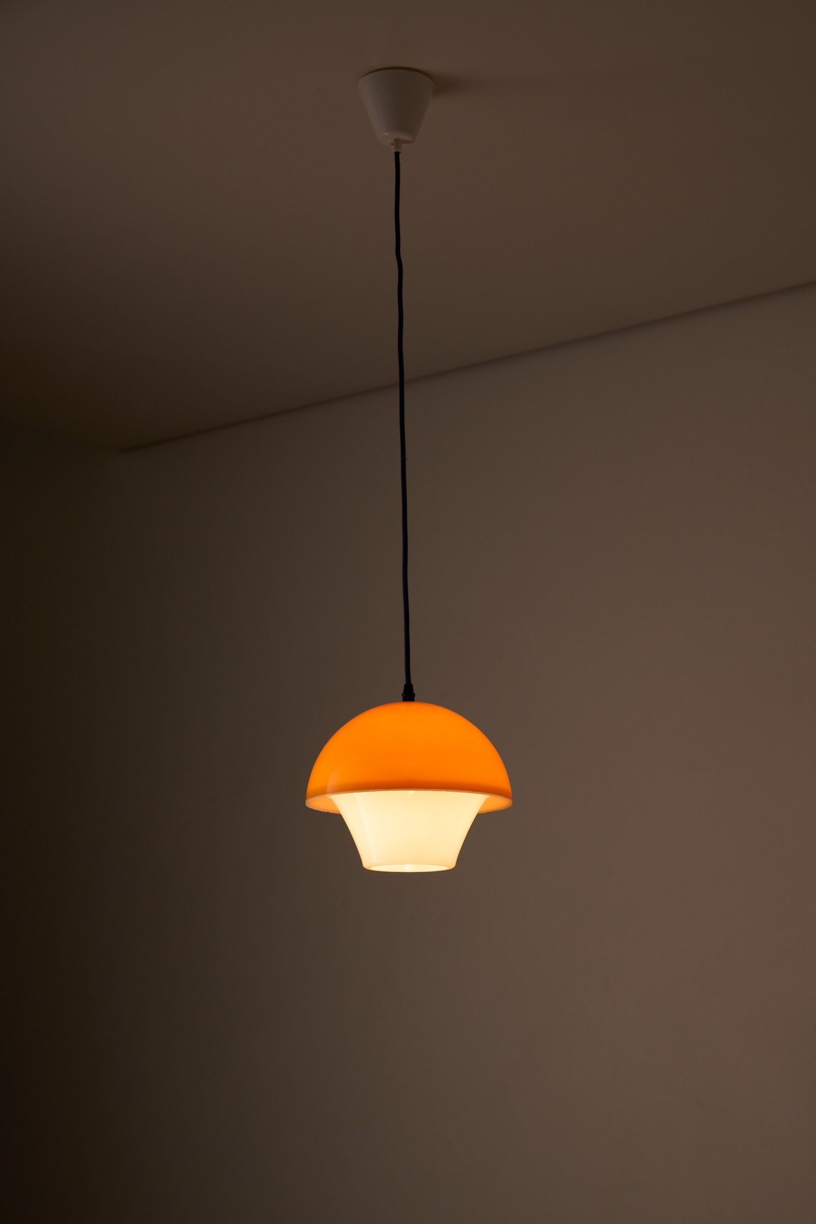 Space Age Mushroom Pendant in Yellow-Orange hanging from the ceiling with a warm light diffusing from its layers.