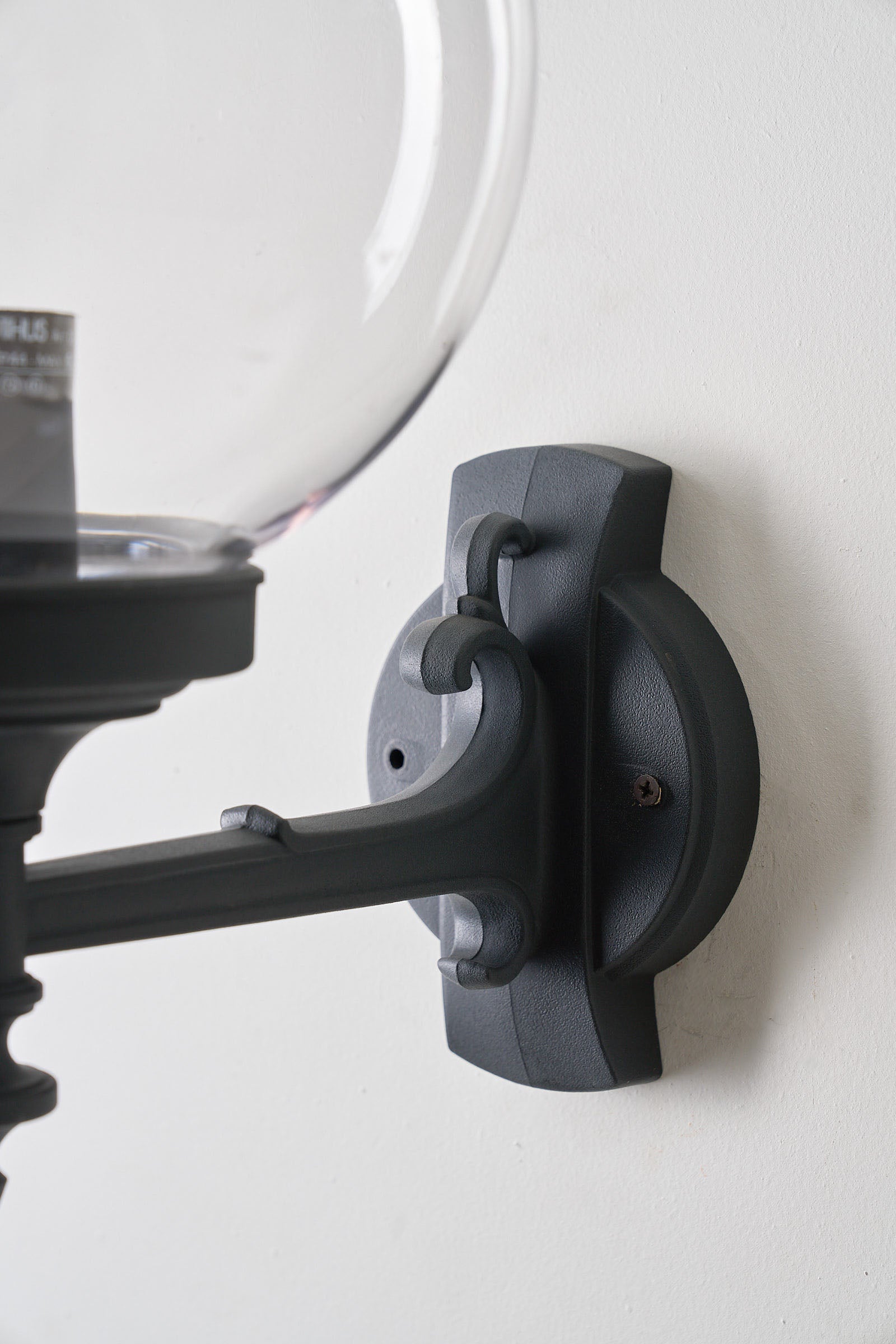 Traditional Outdoor Transparent Spherical Wall Lamp featuring black-lacquered metal bracket against a wall.