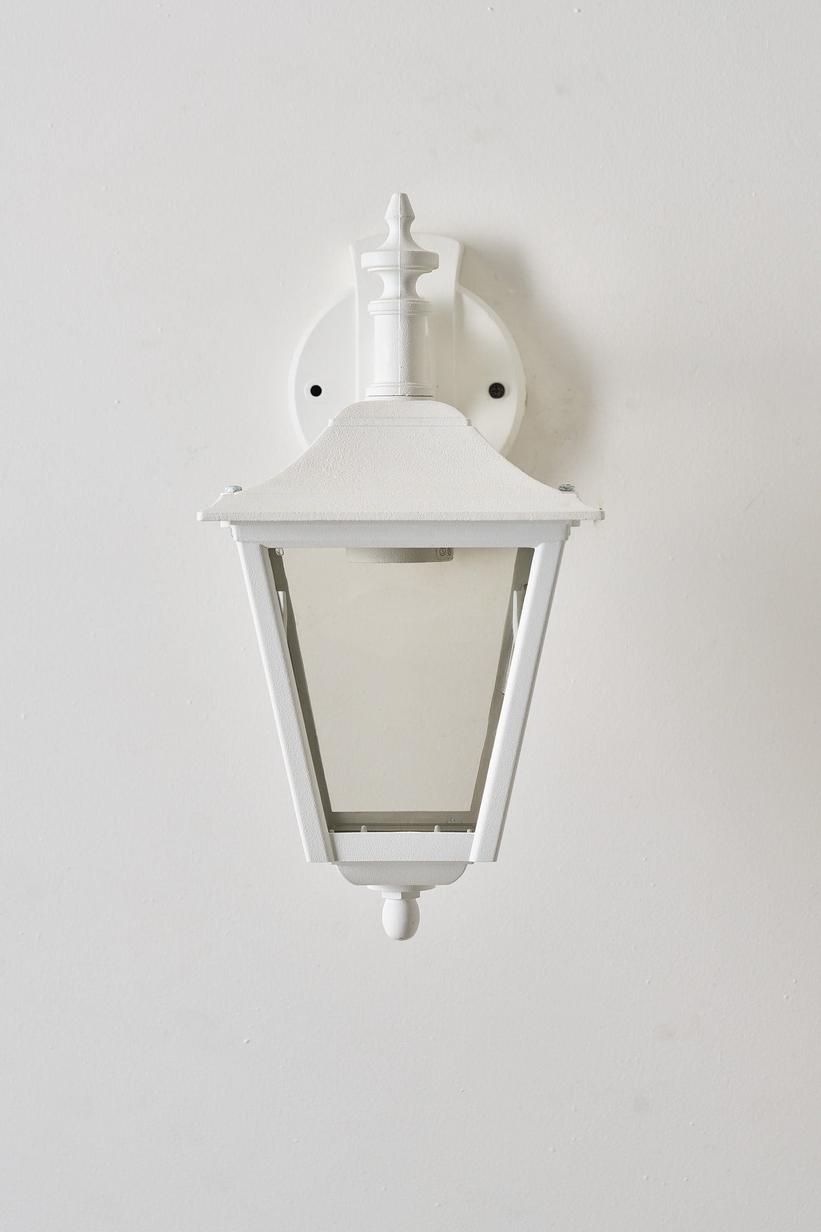 Traditional Outdoor Wall Lantern in White mounted on a wall with clear panes and decorative bracket.