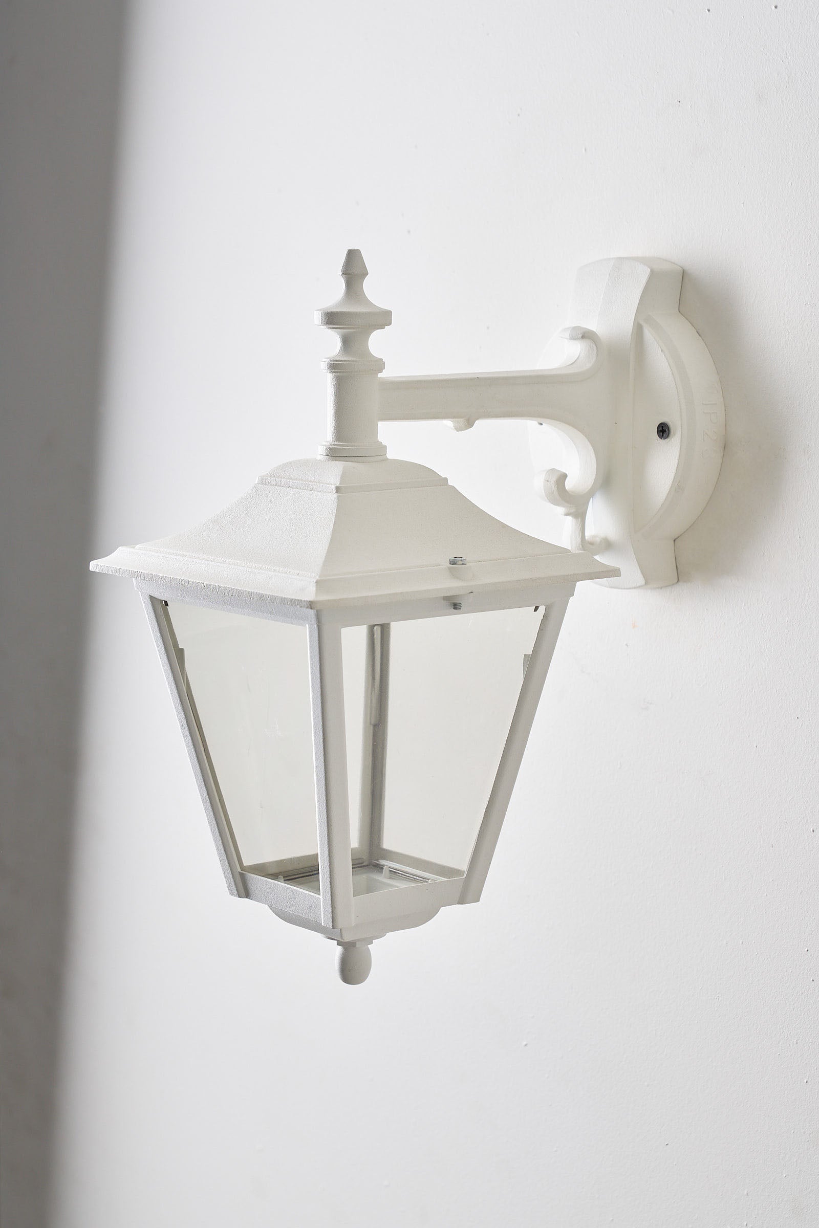 Traditional Outdoor Wall Lantern in White mounted on a wall, featuring a classic carriage silhouette and clear panes.
