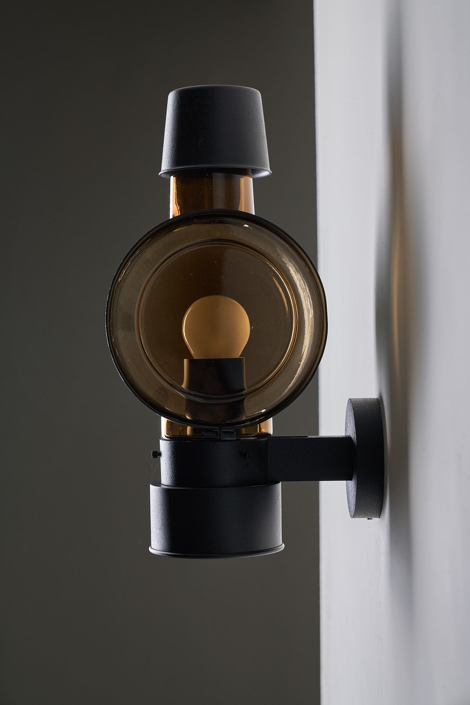 Bega Boom Outdoor Sconce Cylindrical Amber Glass mounted on a wall, showcasing nautical lens design and amber-brown glass.