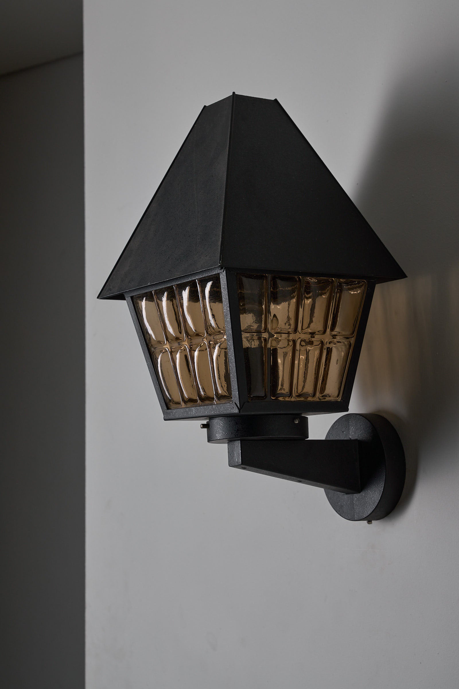 Bega Boom Outdoor Wall Lantern featuring textured amber glass panes and a dark metal body.