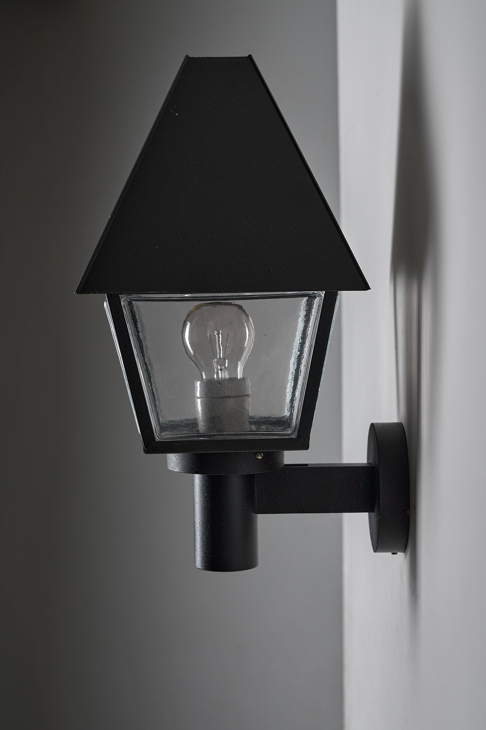 Bega Boom Outdoor Wall Light featuring a minimalist lantern sconce in dark textured metal with glass panels for exterior lighting.