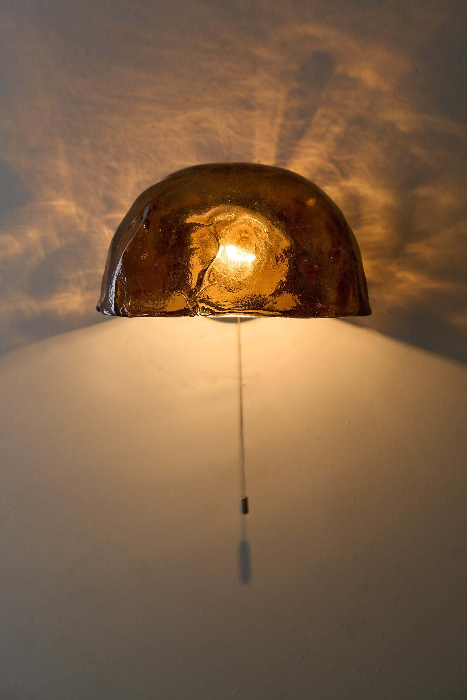 Pair of Kalmar Brown Glass Wall Lamps illuminating a wall with amber light, showcasing textured glass design.