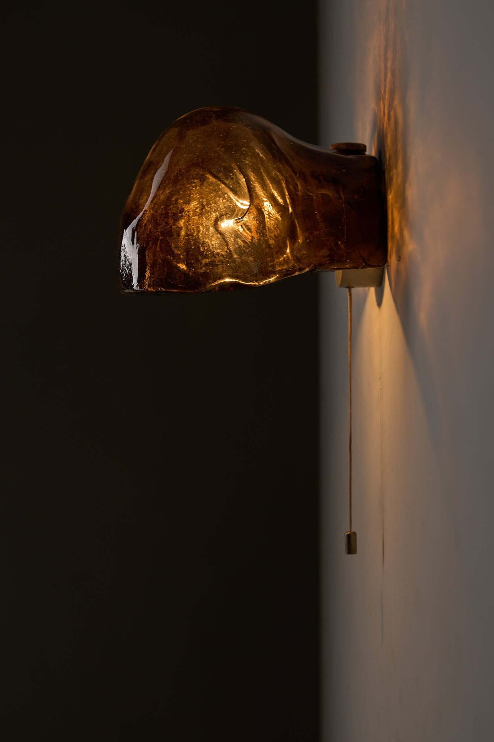 Pair of Kalmar Brown Glass Wall Lamps illuminating a wall with warm amber light, showcasing textured glass design.