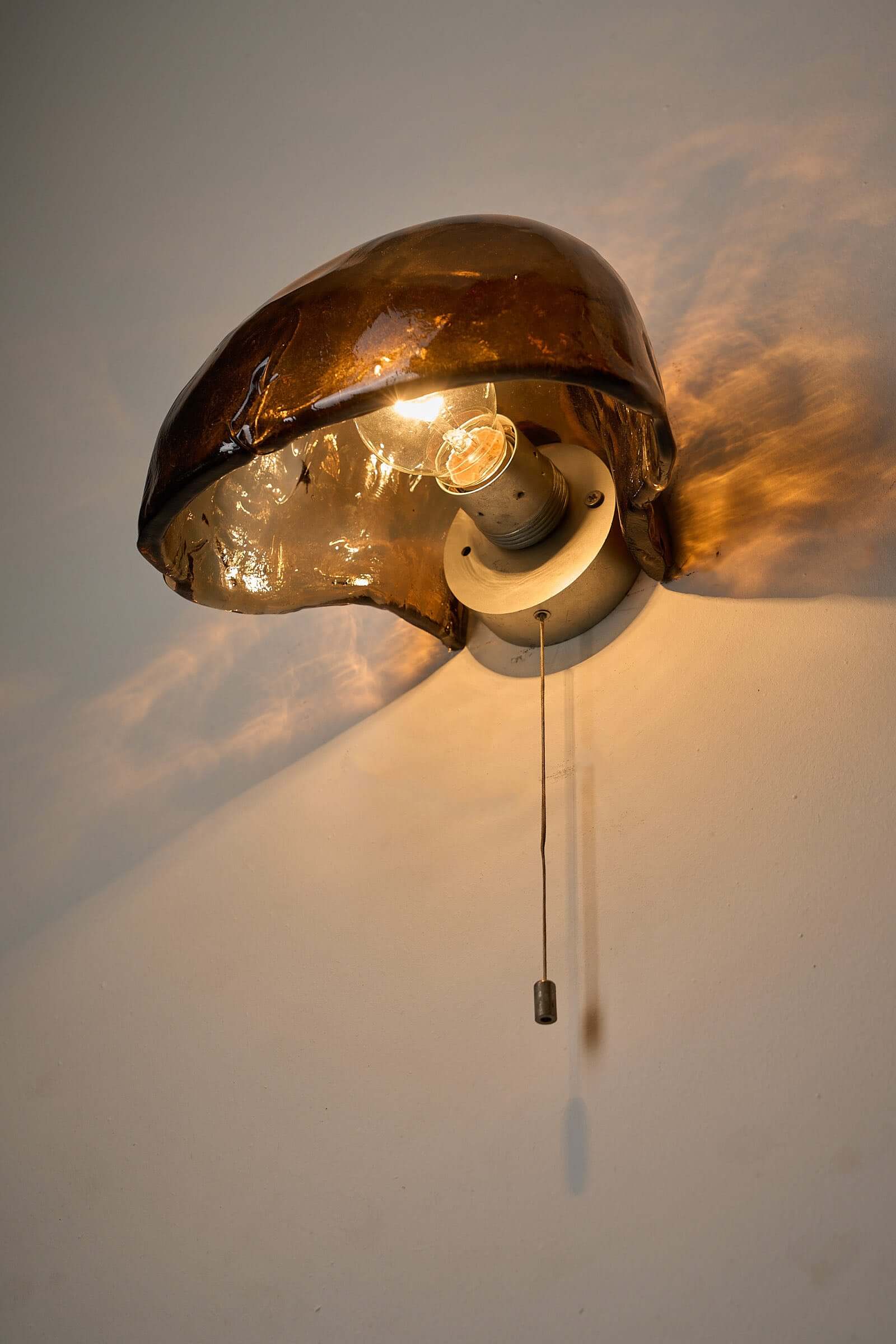 Pair of Kalmar Brown Glass Wall Lamps illuminating a wall with amber light, showcasing textured glass and unique shape.