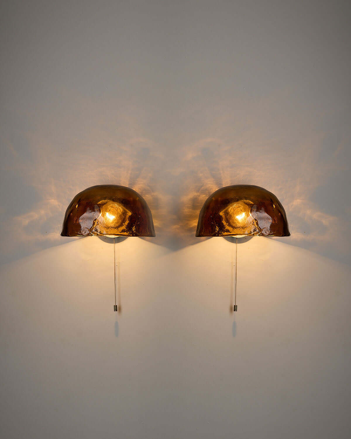 Pair of Kalmar Brown Glass Wall Lamps illuminated against a wall, showcasing their textured amber glass design.