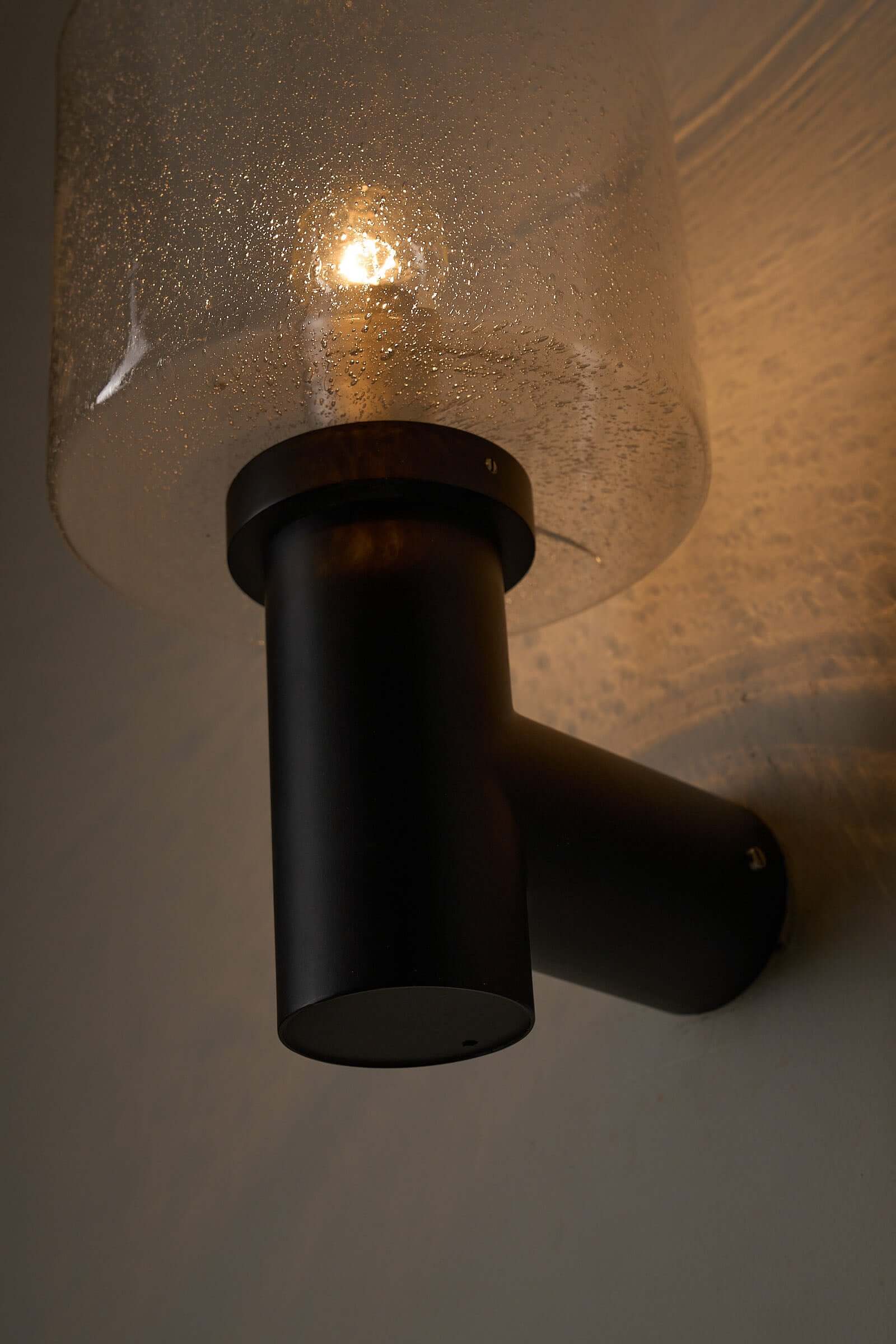 Glashütte Limburg Conical Bubble Glass Outdoor Sconce mounted on wall, featuring smoke-tinted bubble glass and dark metal base.