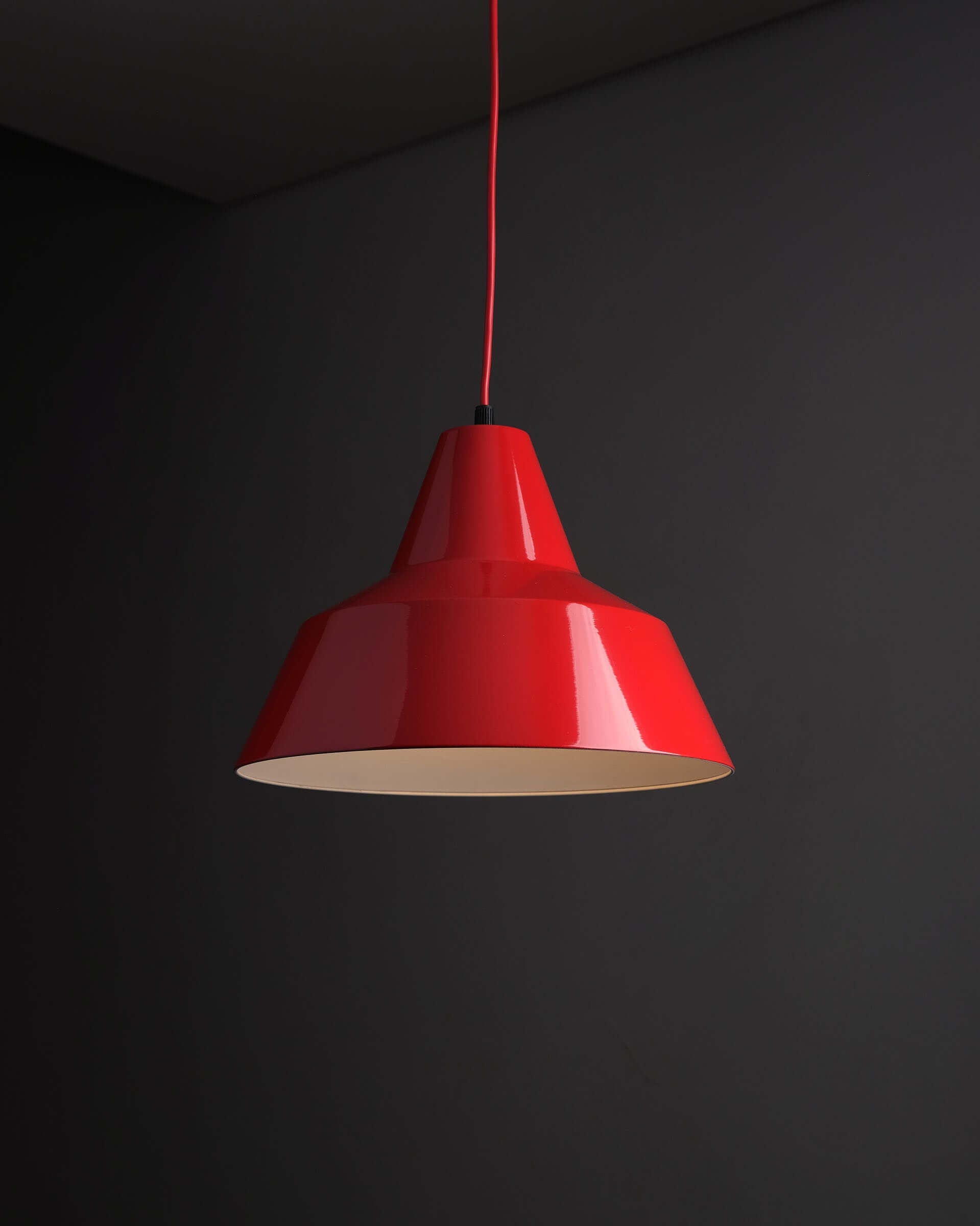 Red Industrial Warehouse Pendant Light by Lyfa hanging from a ceiling against a dark wall.