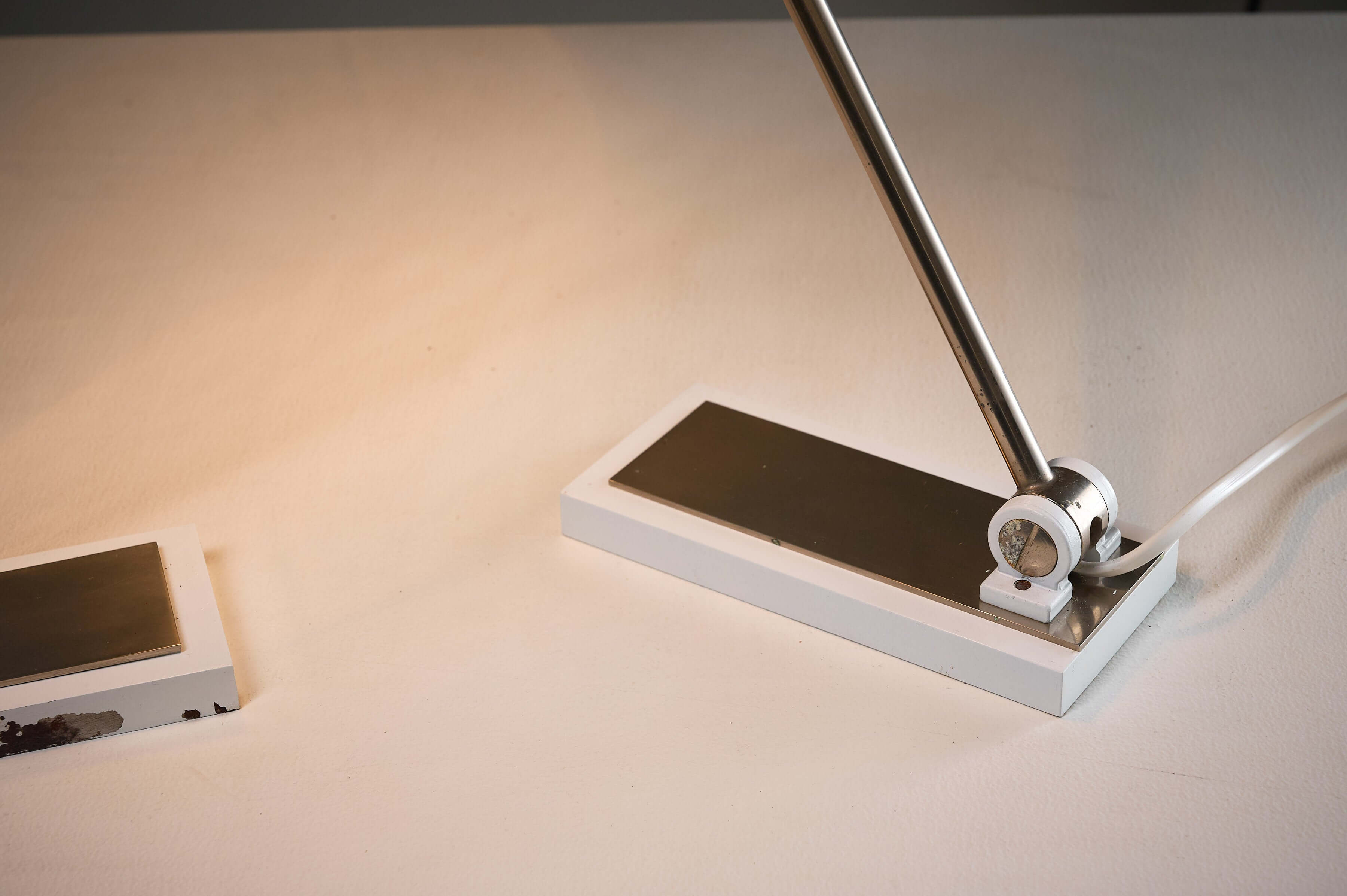 Minimalist White Cylinder Desk Lamp by Artiforte with a chrome stem and rectangular base on a table.