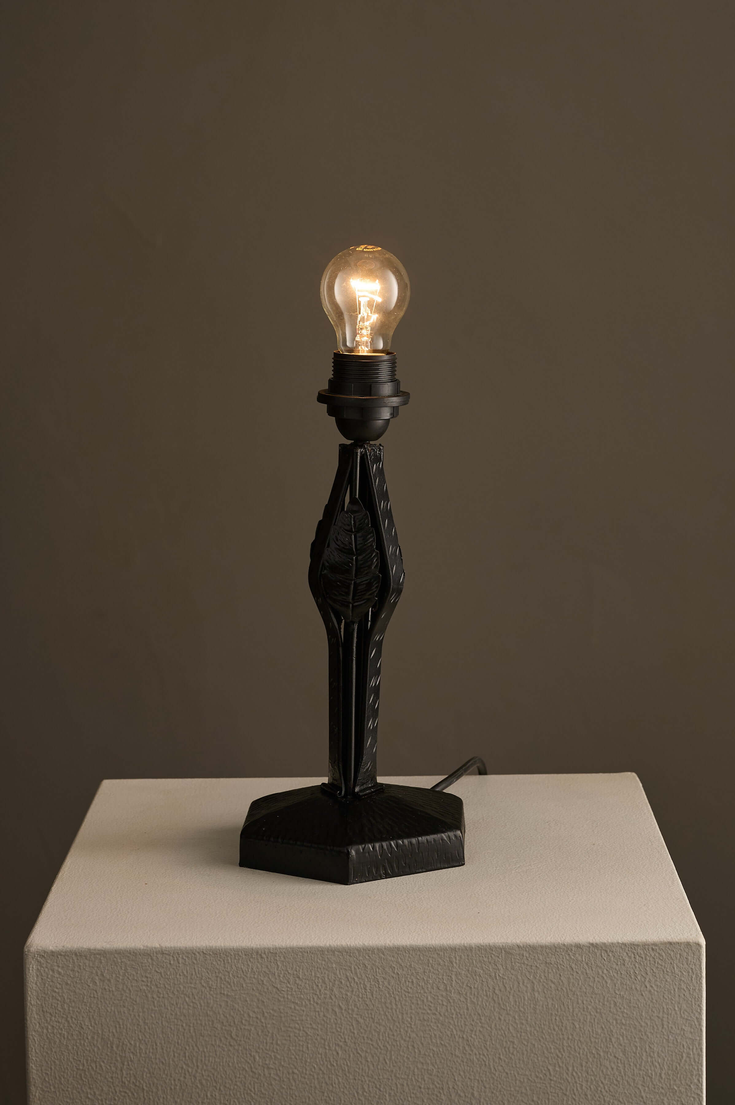 Black Hammered Metal Table Lamp with Stylized Leaf Motif on a pedestal, showcasing an industrial design and hammered texture.