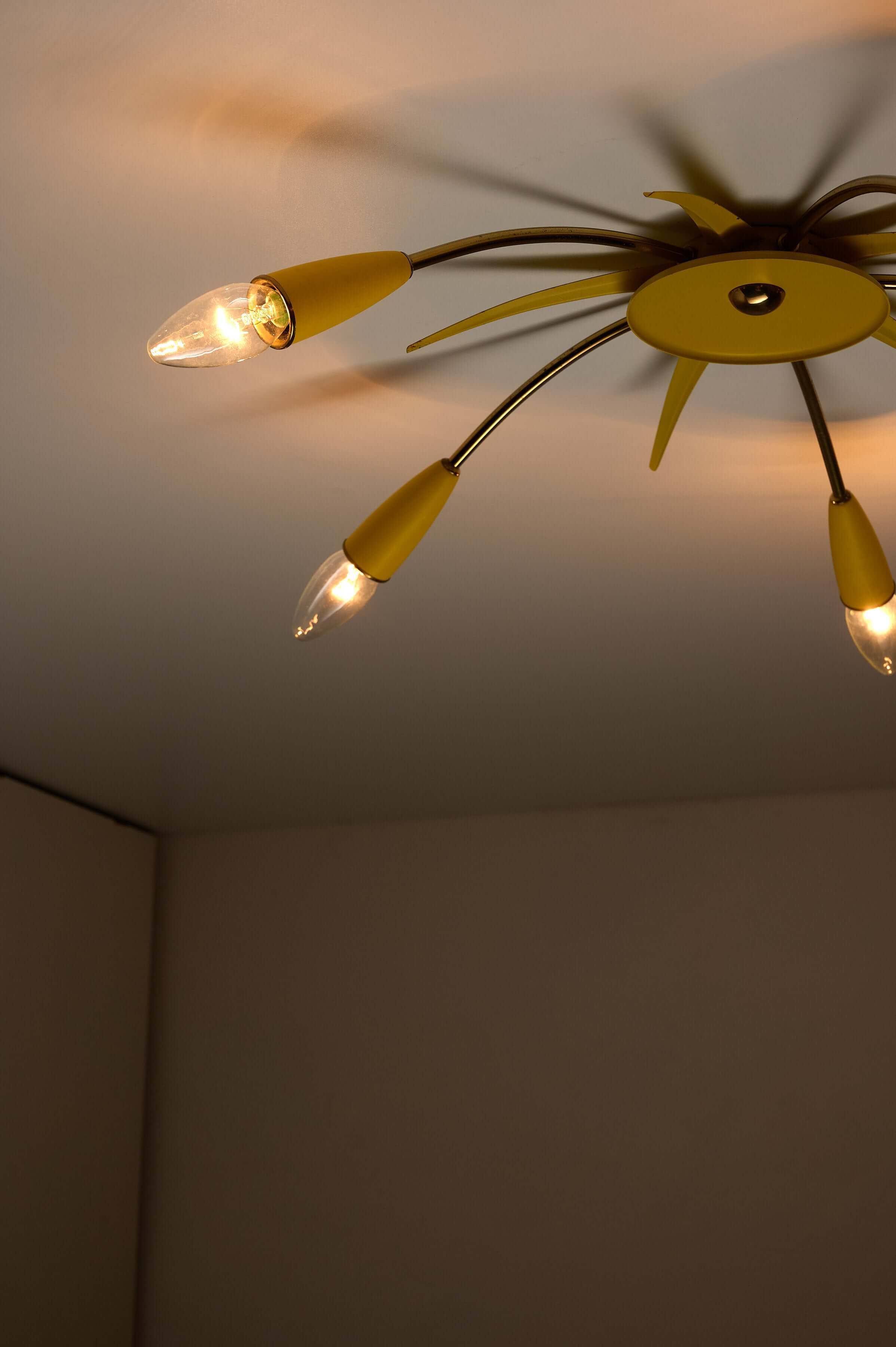 Mid-Century Yellow Sputnik Ceiling Lamp featuring a starburst design and brass arms, illuminating a room.