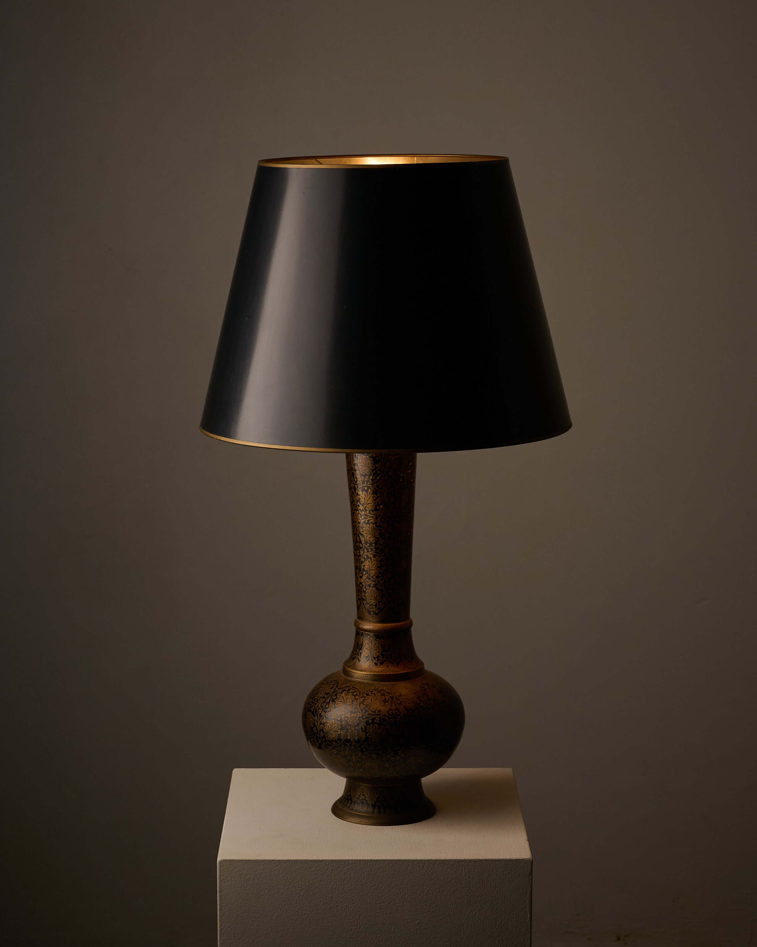 Tall Black and Gold Vase Lamp with Foliage Pattern on a pedestal against a dark background.