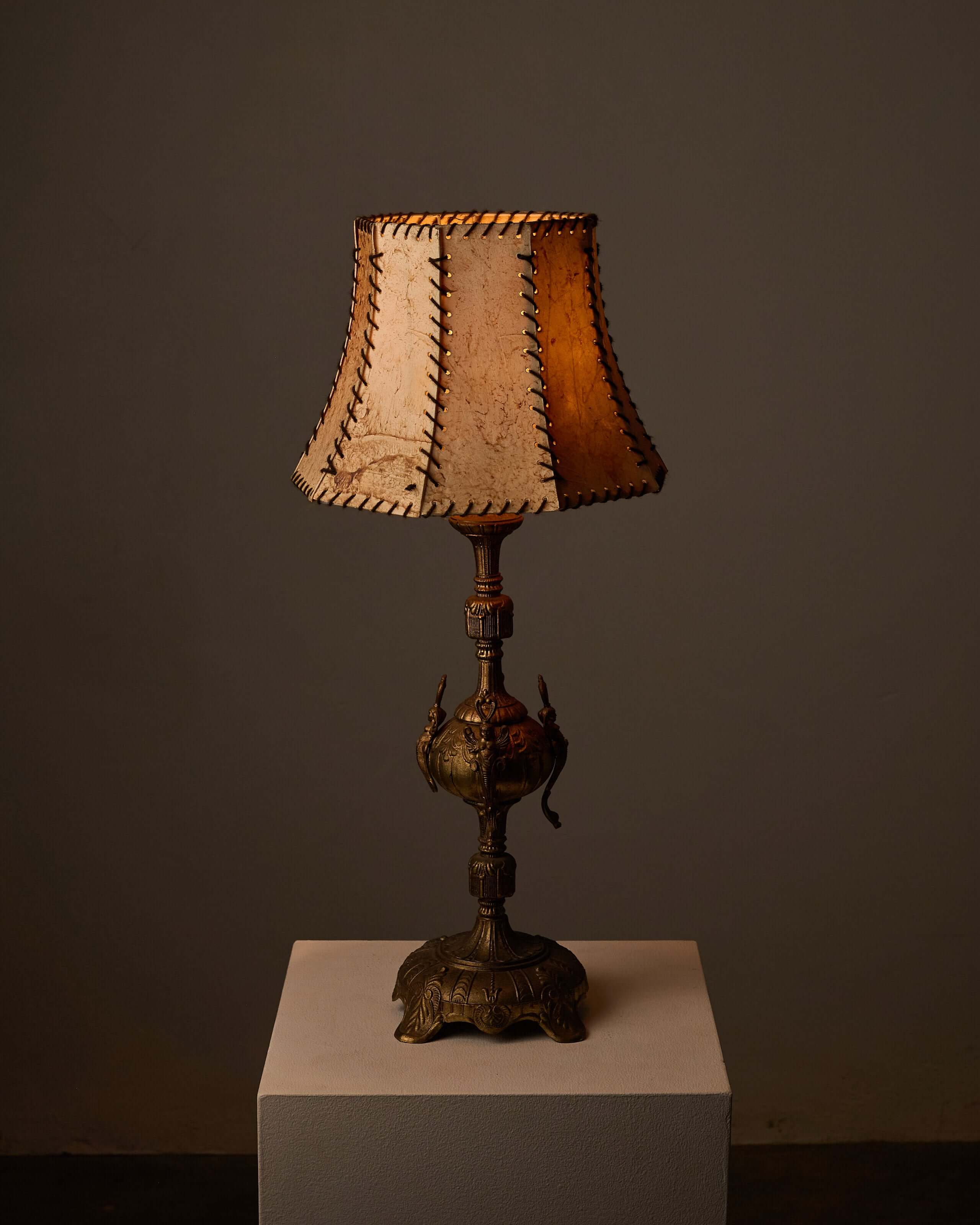 Cast Brass Table Lamp with Stitched Parchment Shade on a pedestal, featuring intricate detailing and warm lighting.
