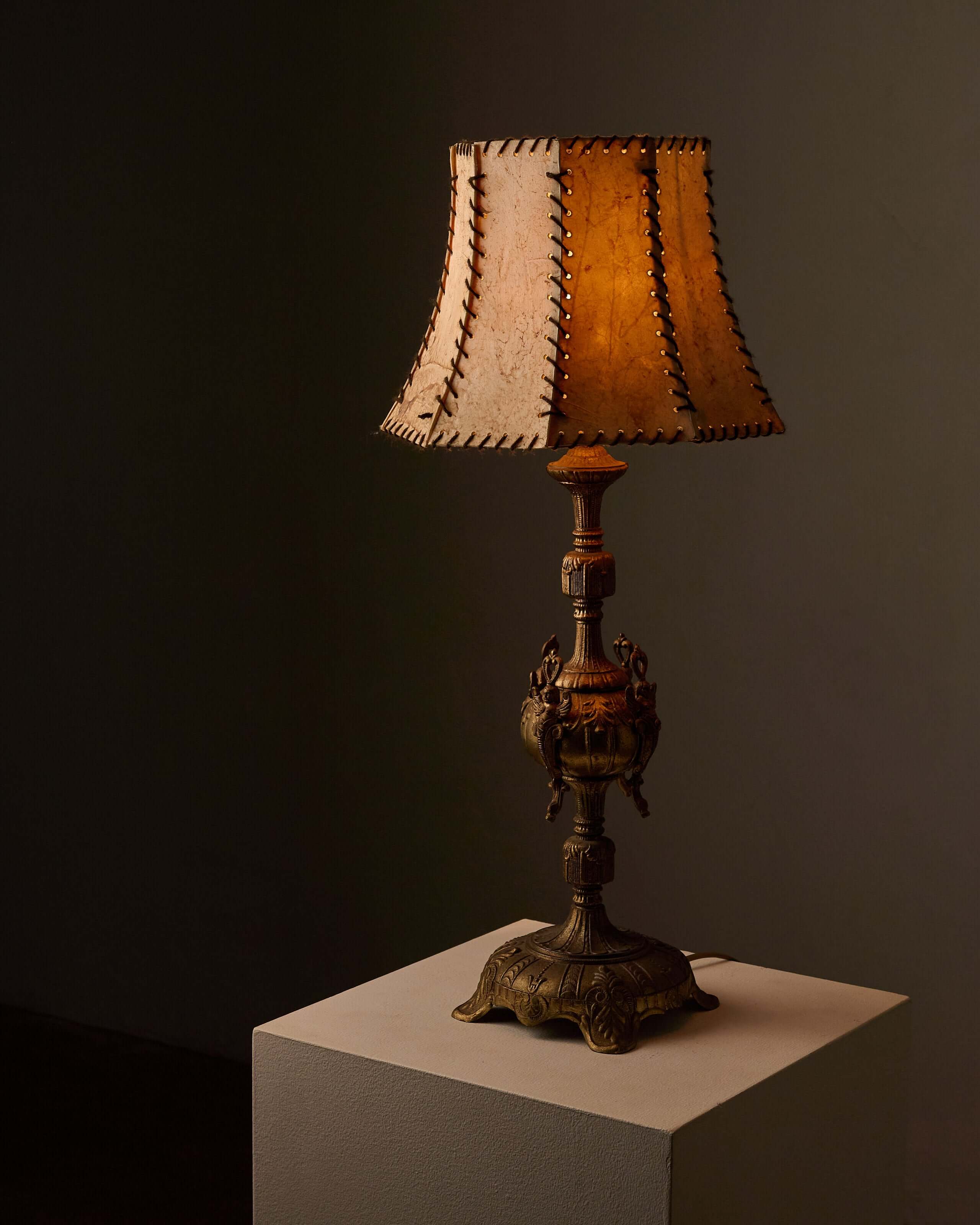 Cast Brass Table Lamp with Stitched Parchment Shade featuring intricate winged figures and whip-stitching on the shade.