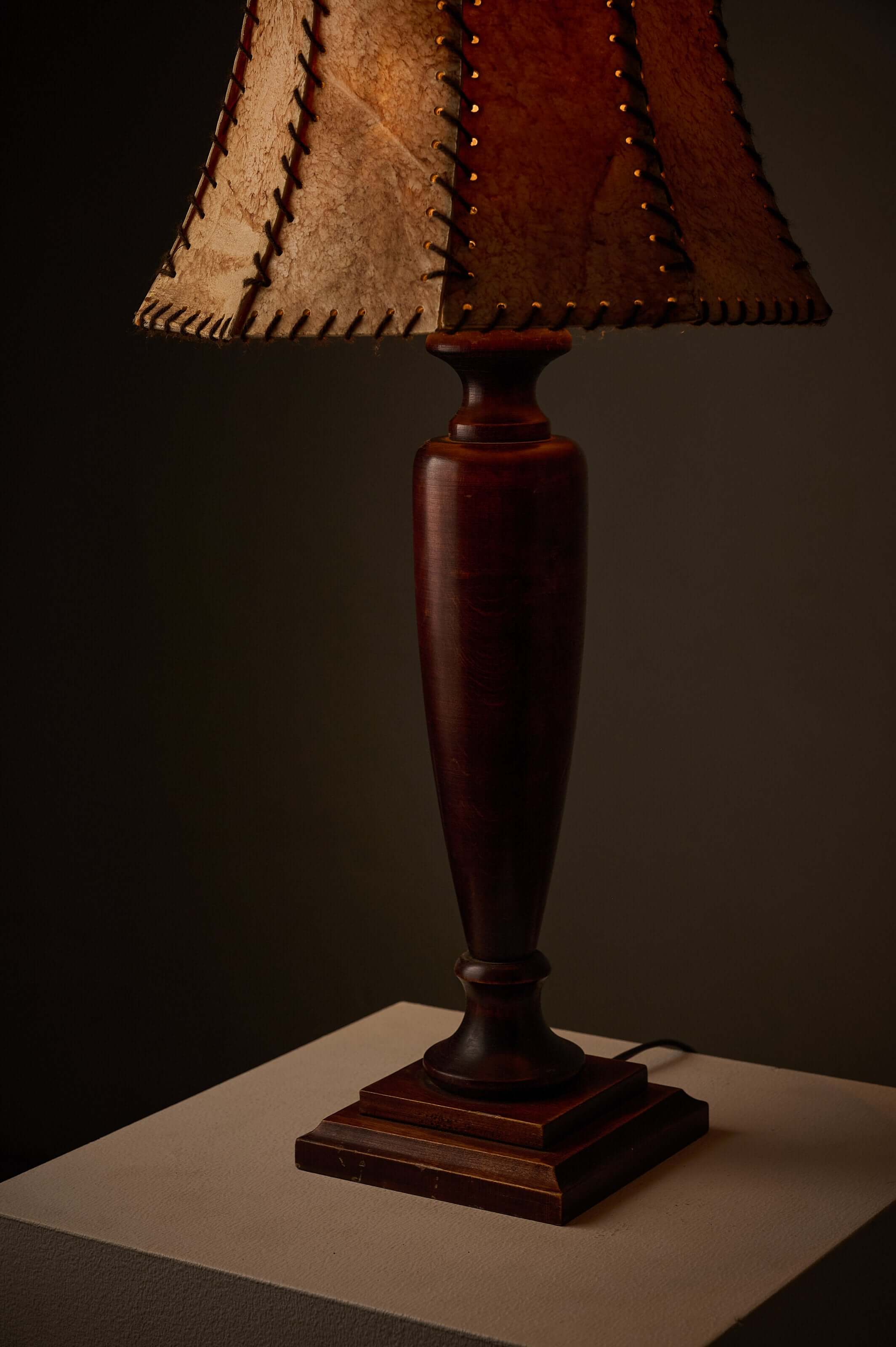 Turned dark wood table lamp with stitched shade showcasing rustic appeal and classical proportions.
