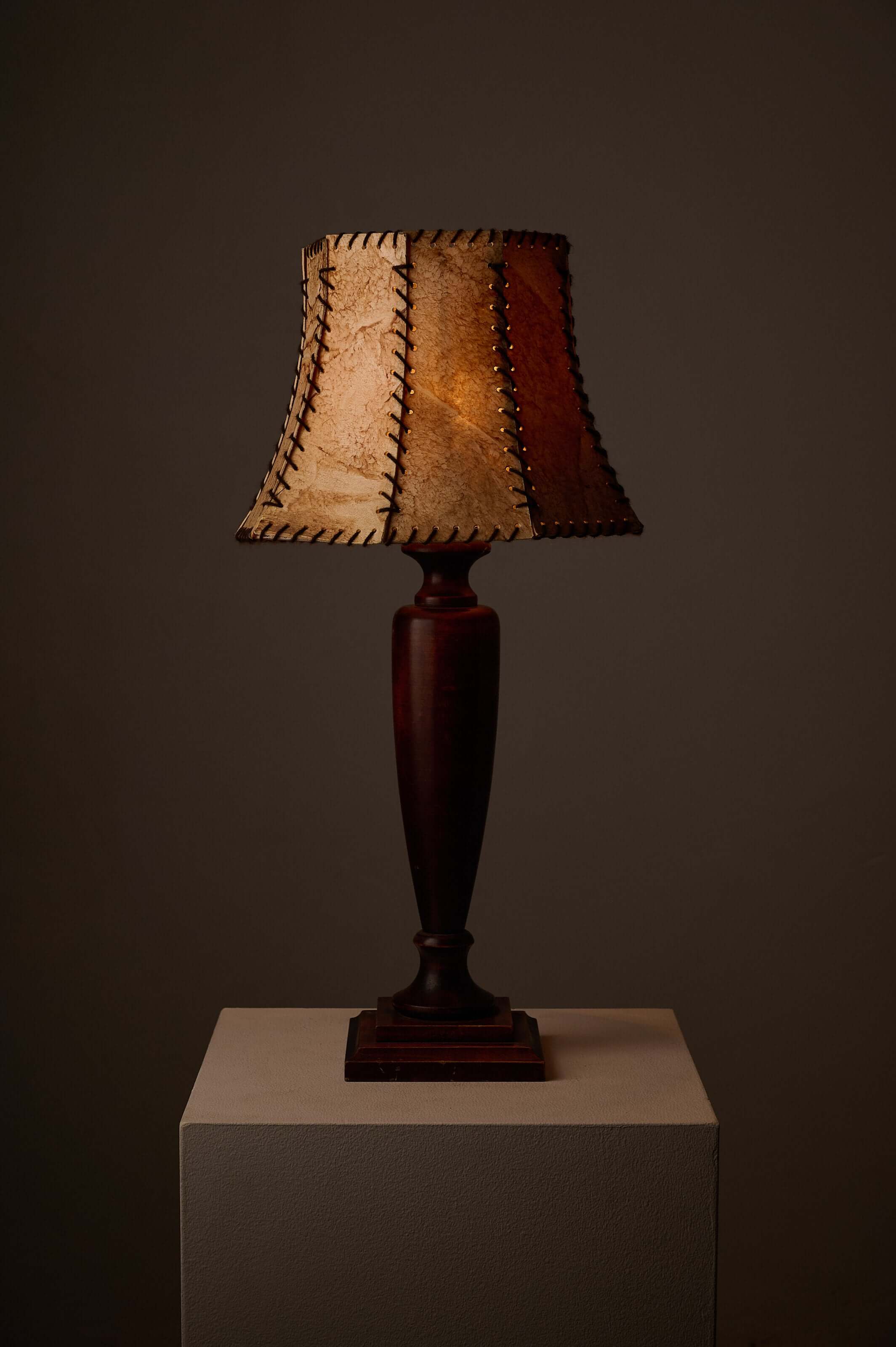 Turned dark wood table lamp with stitched shade on a pedestal, showcasing warm rustic appeal.