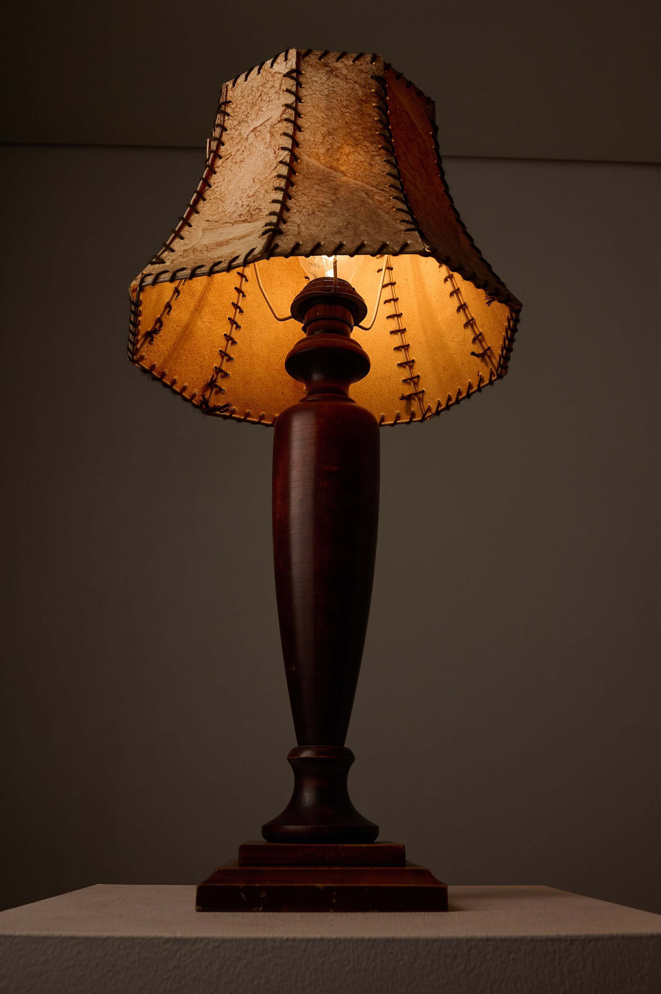 Turned dark wood table lamp with stitched shade, showcasing warm light and rustic design.