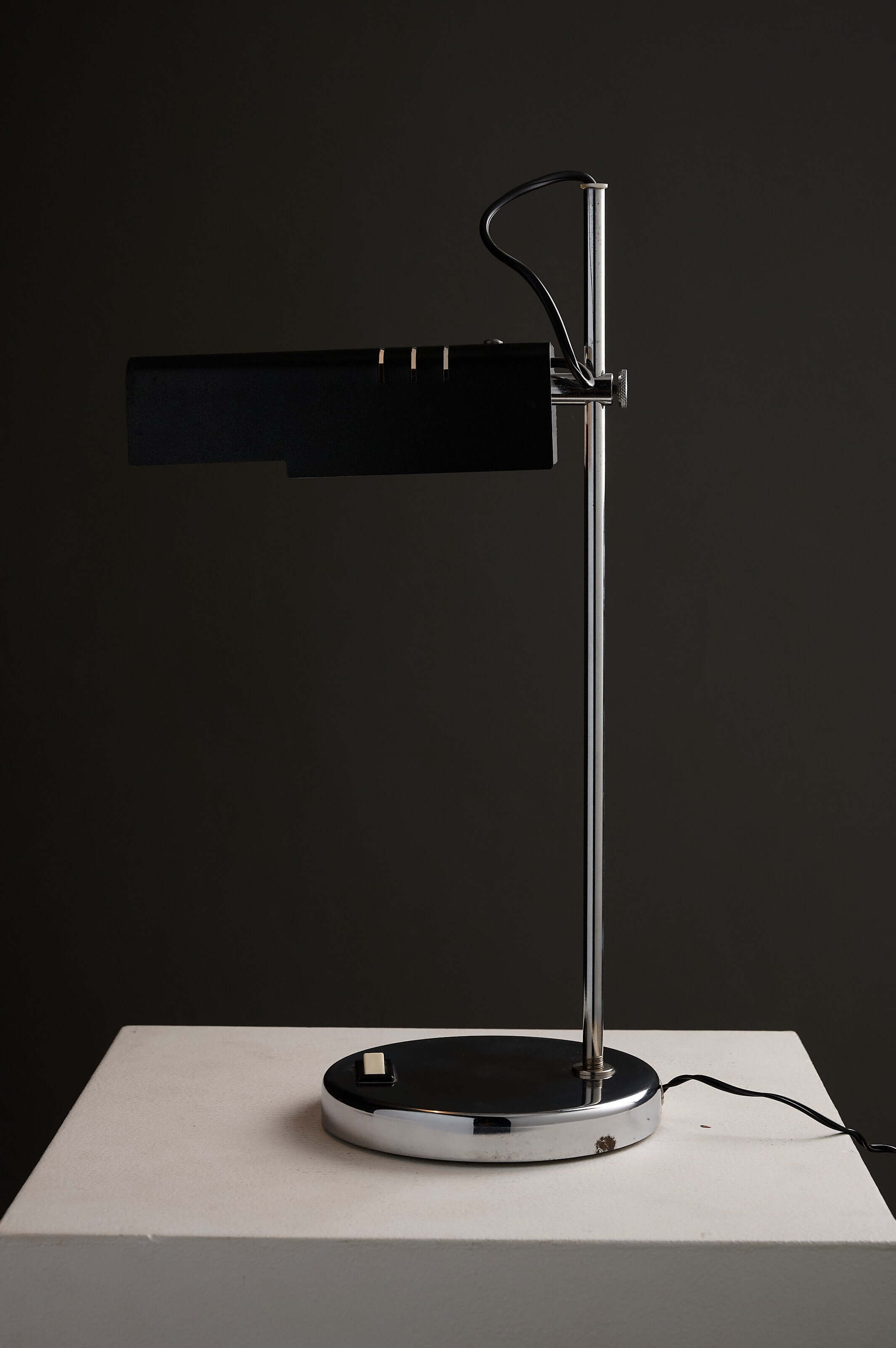 Adjustable chrome desk lamp with a folded black shade and a sleek chrome stem on a circular base.