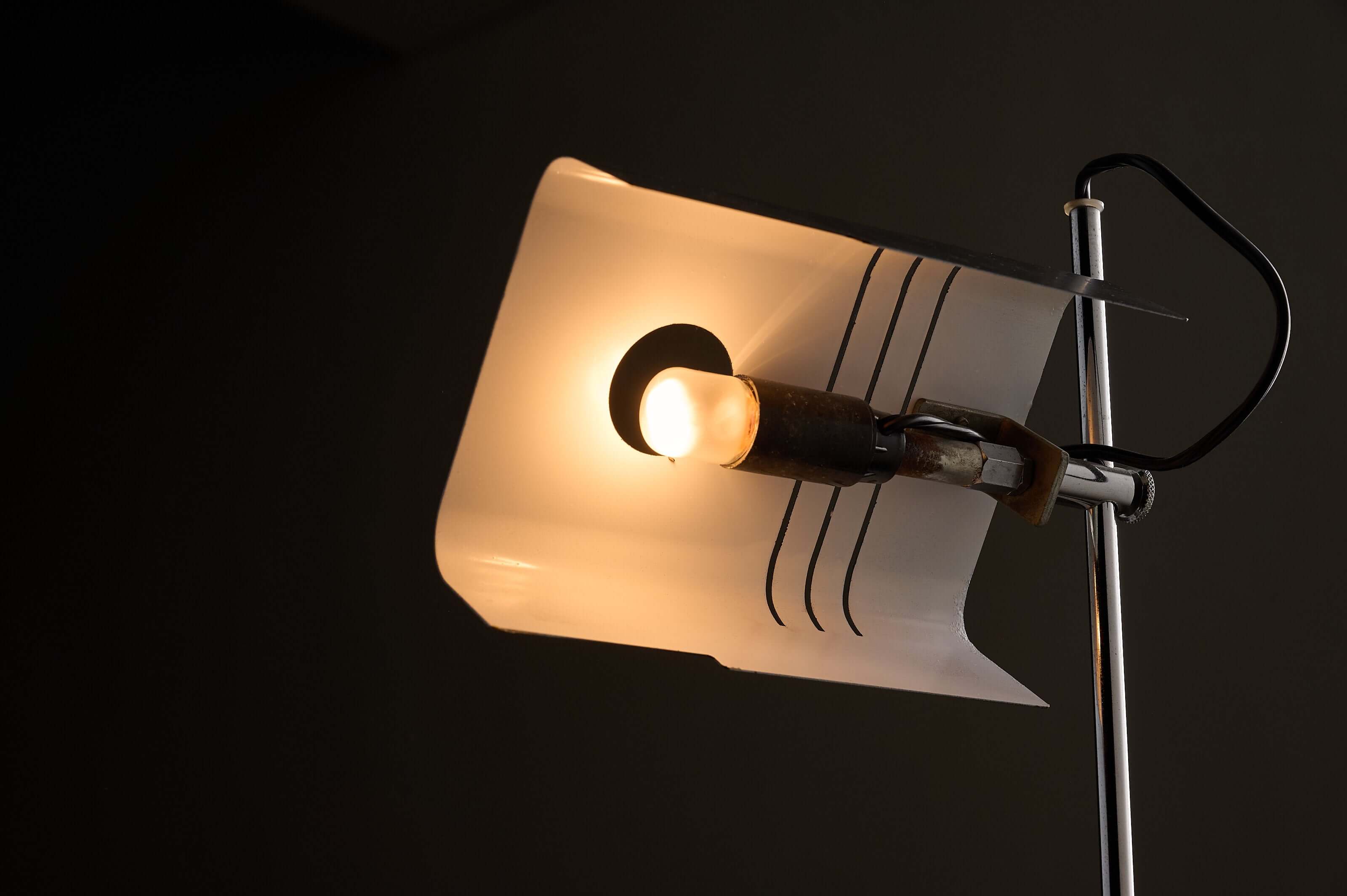 Adjustable chrome desk lamp with a unique folded metal shade illuminating a warm light.